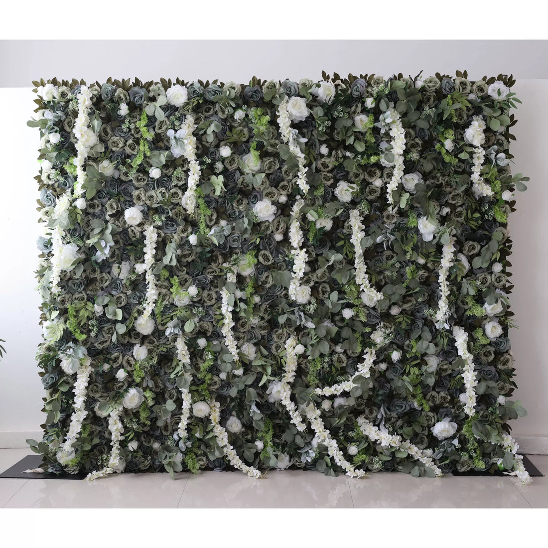 This large artificial greenery wall features a dense mix of dark green foliage, white roses, and trailing white flowers. A blue circle stands out in the center, adding a unique focal point. The lush, layered arrangement creates a natural - looking, elegant backdrop, perfect for events or decor.