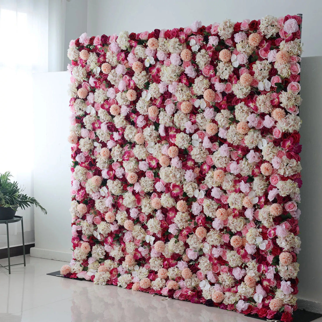This is a large artificial flower wall. It combines red blossoms with white, pink, and peach - colored blooms, creating a rich, textured display. The dense arrangement of varied flowers, like hydrangeas and roses, forms a vibrant, eye - catching backdrop, perfect for adding an elegant, decorative touch to events such as weddings or parties.