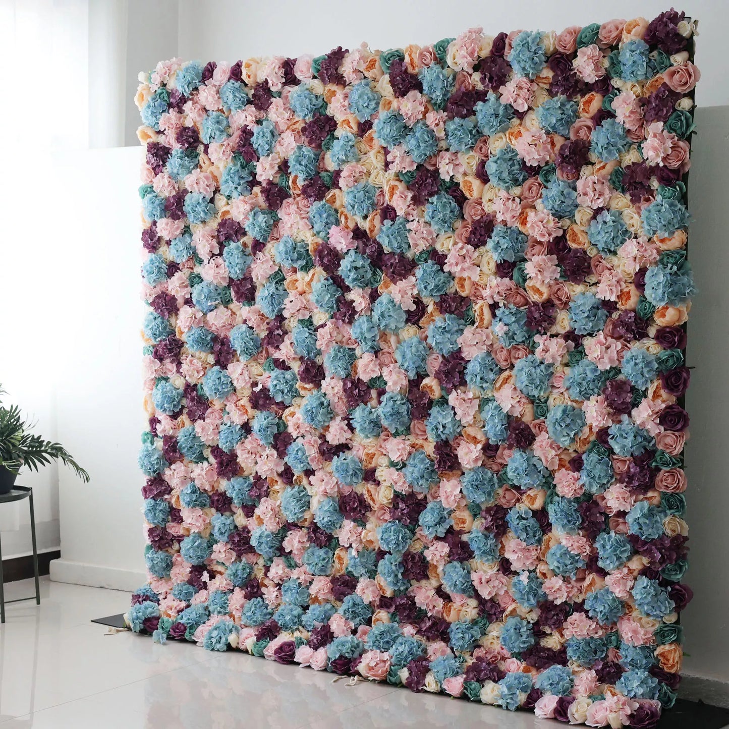 Valar Flowers Roll Up Backdrop: This is a large artificial flower wall. It showcases a vibrant mix of colors—soft pinks, blues, purples, and creams. Densely packed with varied blooms, it creates a lush, textured tapestry. Perfect for event backdrops, adding a colorful, elegant touch to weddings or parties, enhancing the decorative appeal of any space. 