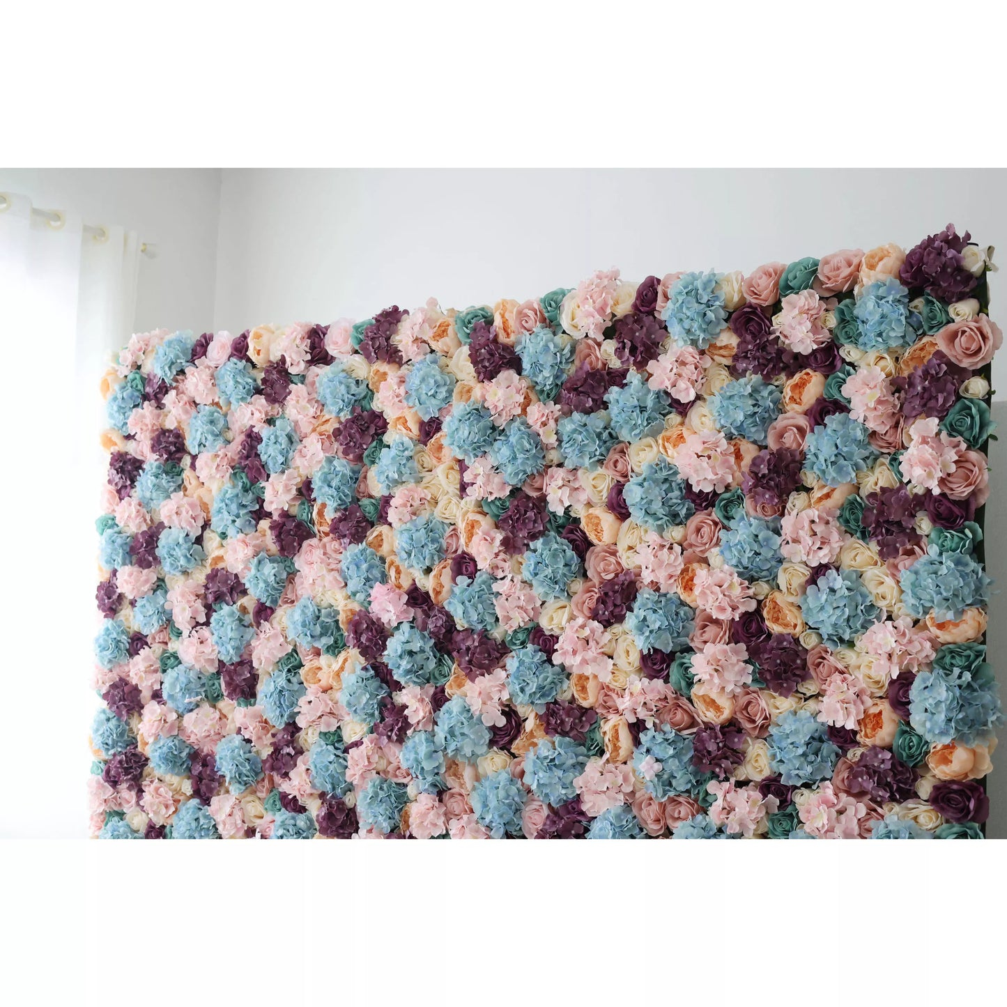 This is a large artificial flower wall, a vibrant tapestry of pastel hues—soft pinks, blues, purples, and creams. Densely packed with varied blooms like hydrangeas and roses, it creates a lush, textured display. Perfect for event backdrops, adding an elegant, colorful touch to weddings or parties, enhancing the decorative appeal of any space. 