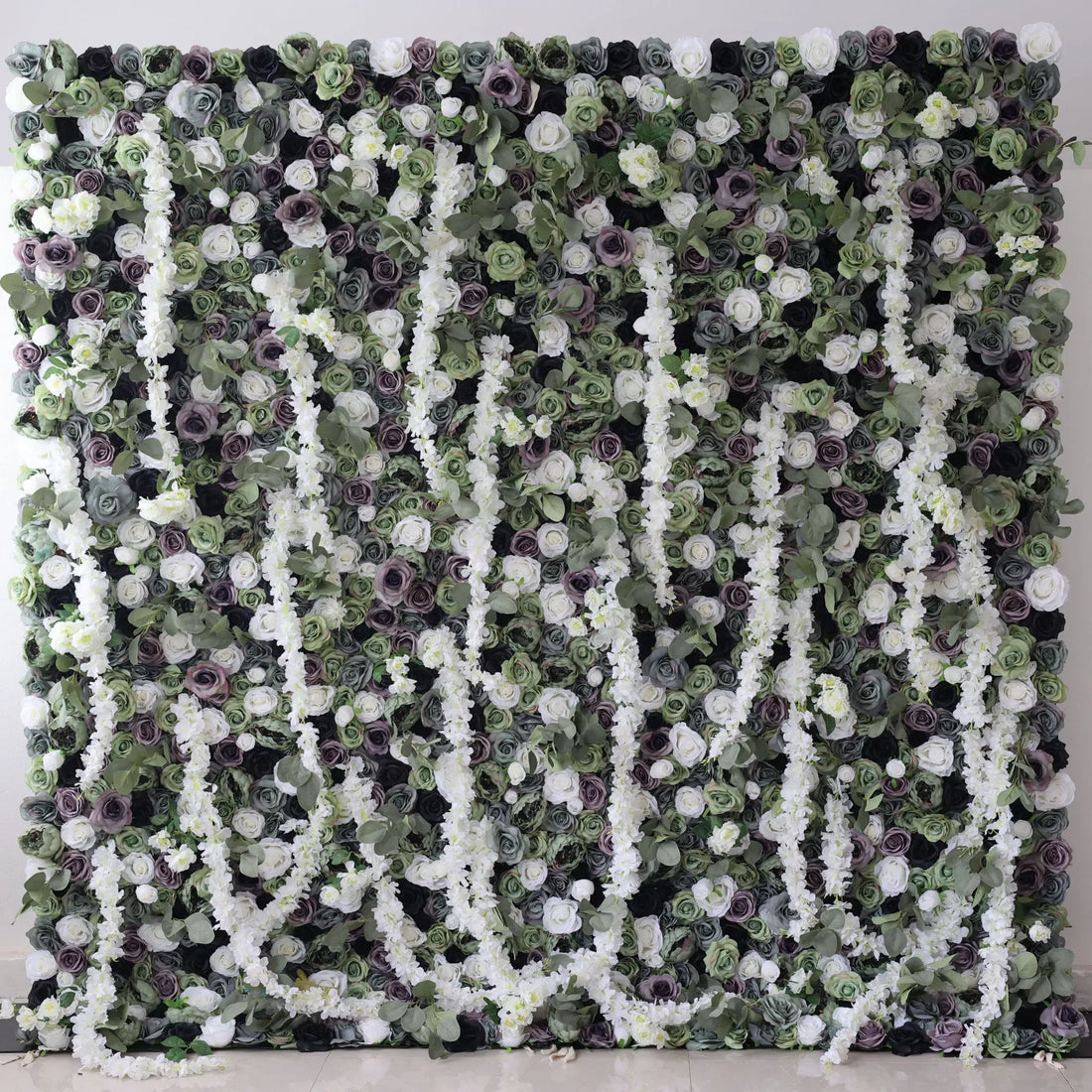 This is a large artificial flower wall with a green - dominated color scheme. It features white blossoms, purple roses, and dense green foliage. The arrangement includes cascading white floral vines, creating a lush, natural - looking display. Ideal for decorative event backdrops, adding an elegant and verdant touch.