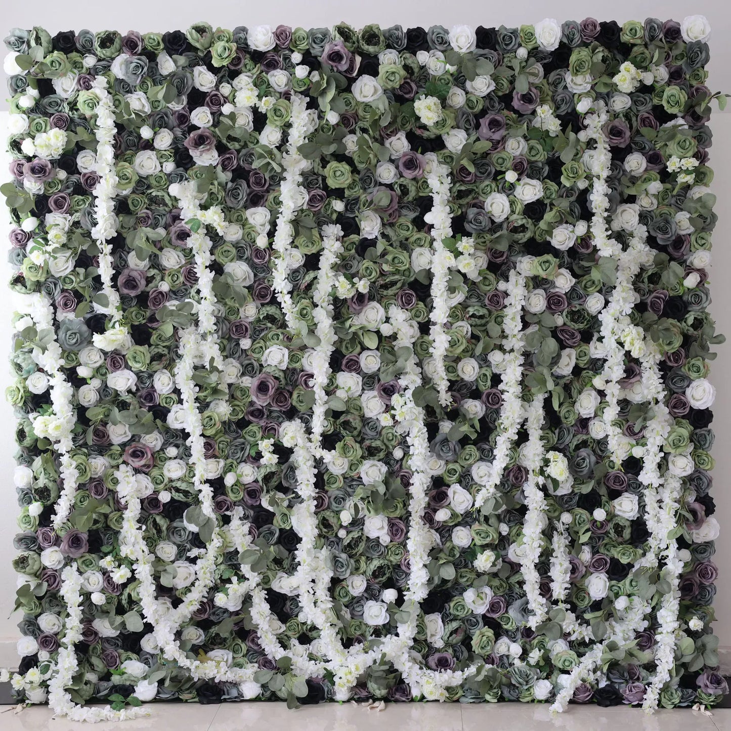This is a large artificial flower wall with a green - dominated color scheme. It features white blossoms, purple roses, and dense green foliage. The arrangement includes cascading white floral vines, creating a lush, natural - looking display. Ideal for decorative event backdrops, adding an elegant and verdant touch. 