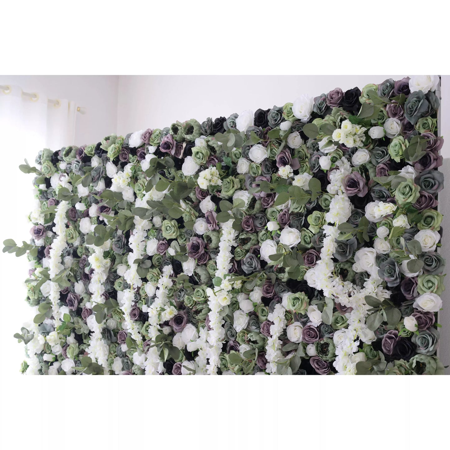 This is a large artificial flower wall with a lush, green - dominated palette. It features white blossoms, purple roses, and varied green foliage. The dense arrangement, including cascading white vines, creates an elegant, natural - looking display, ideal for decorative event backdrops. 