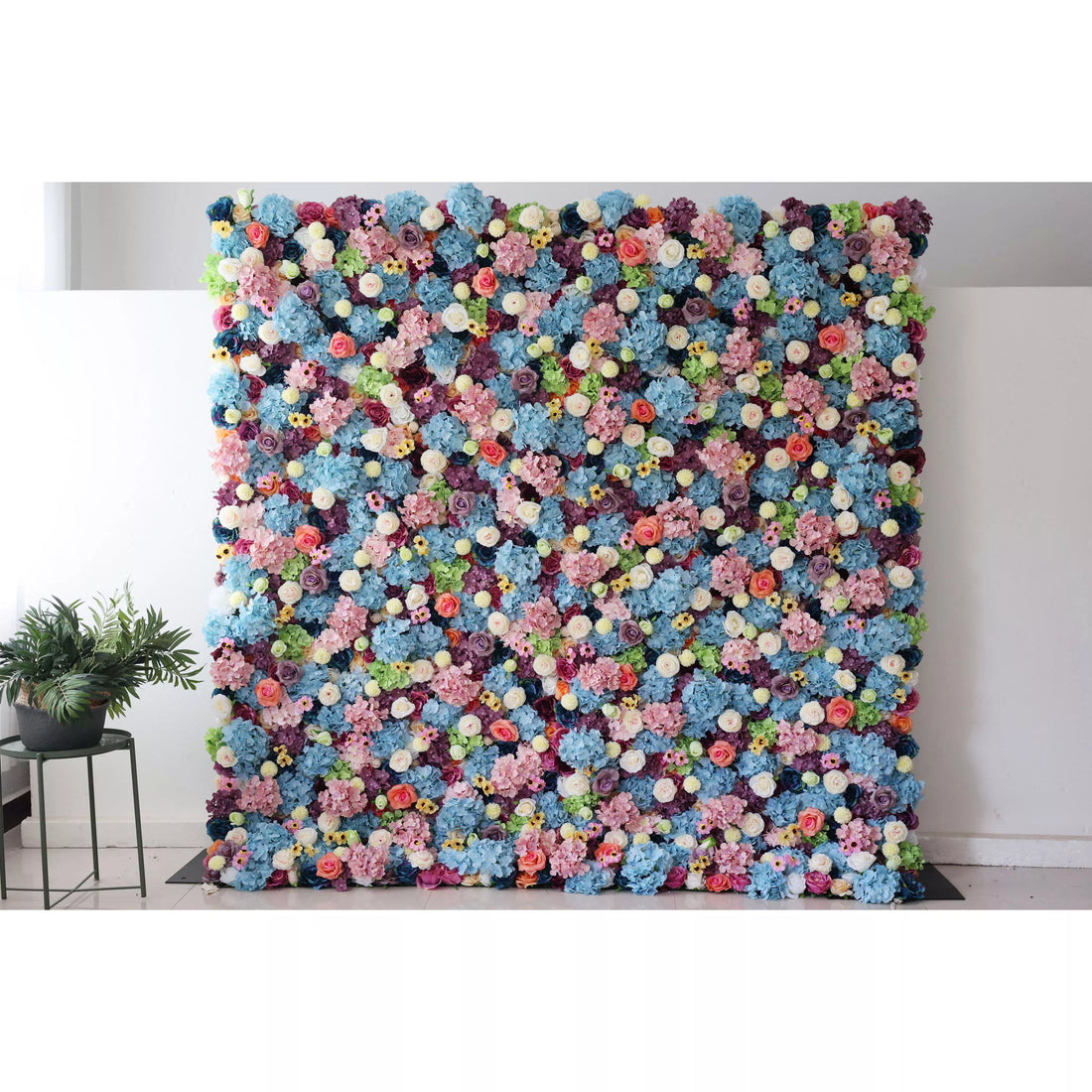 This is a large, vibrant artificial flower wall. It features a dense mix of blue hydrangeas, white roses, pink blossoms, yellow flowers, and green foliage. The colorful, lush arrangement creates a lively, eye - catching display, perfect for event backdrops, adding a cheerful and decorative touch to any space.