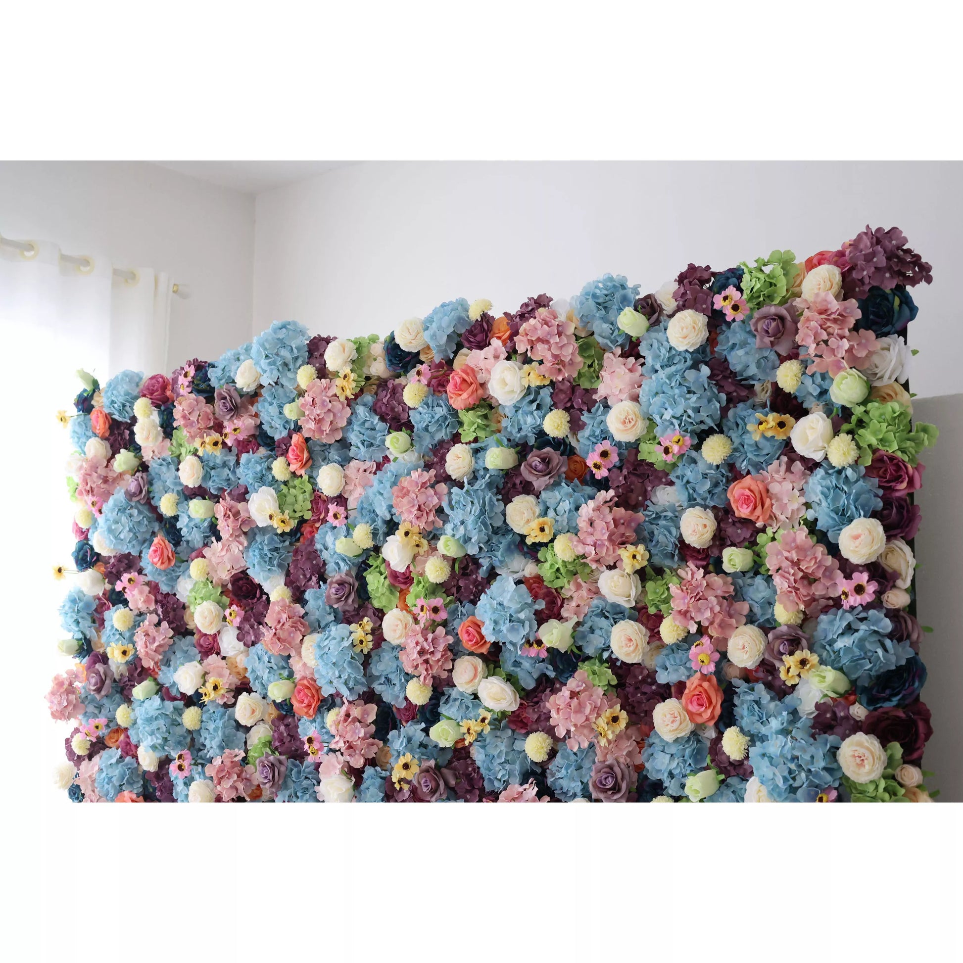 This is a large, vibrant artificial flower wall. It features a dense mix of blue hydrangeas, white roses, pink blossoms, yellow flowers, and green foliage. The colorful, lush arrangement creates a lively, eye - catching display, perfect for event backdrops, adding a cheerful and decorative touch to any space. 