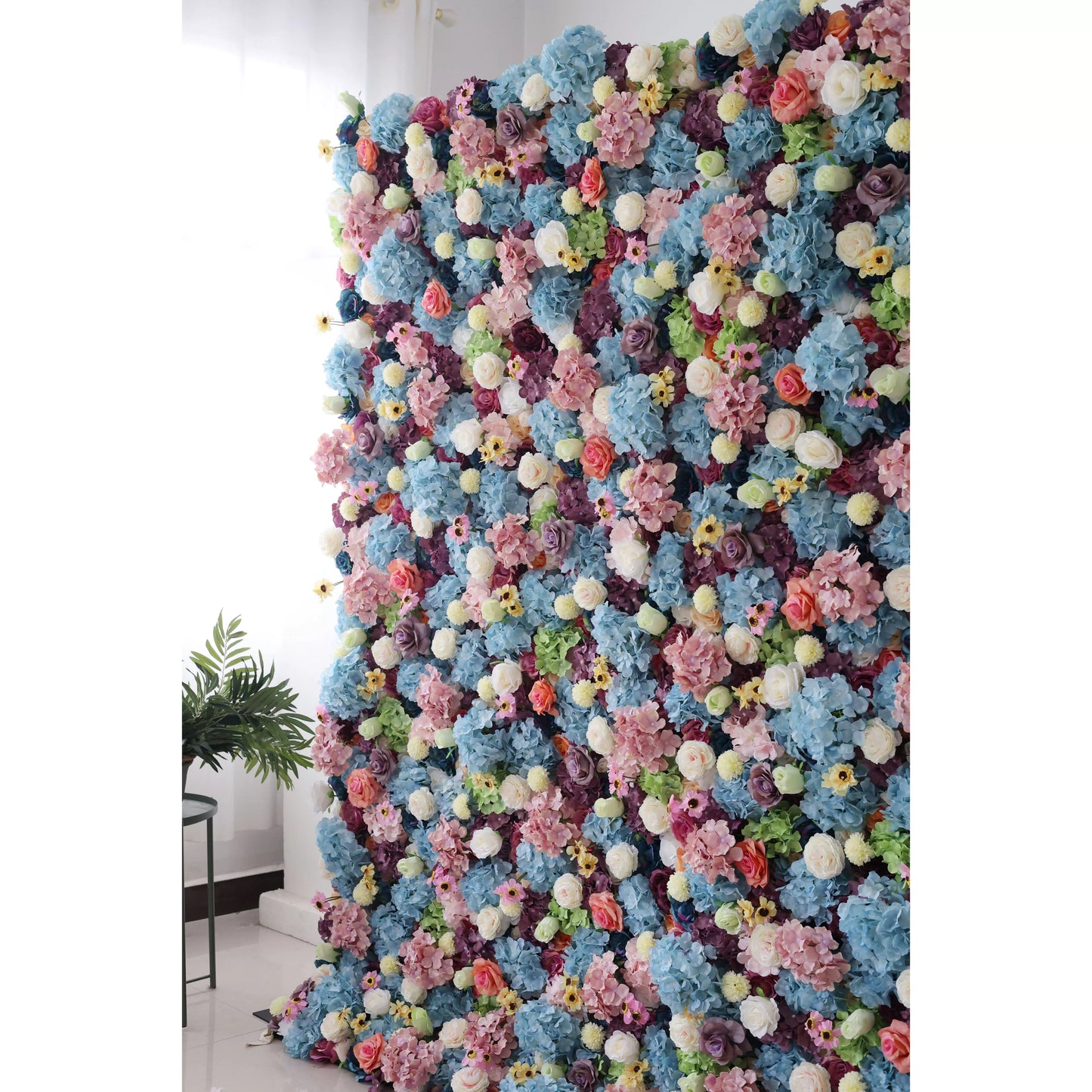 This is a large, vibrant artificial flower wall. It features a dense mix of blue hydrangeas, white roses, pink blossoms, yellow flowers, and green foliage. The colorful, lush arrangement creates a lively, eye - catching display, perfect for event backdrops, adding a cheerful and decorative touch to any space. 