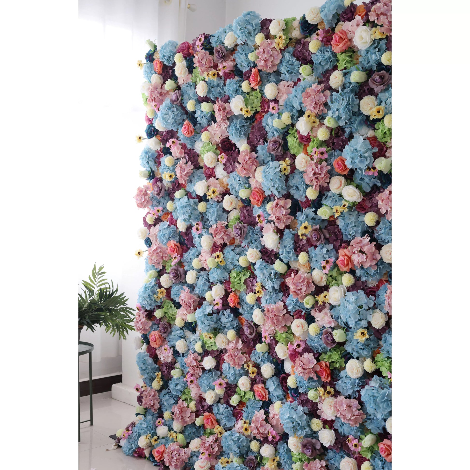 This is a large, vibrant artificial flower wall. It features a dense mix of blue hydrangeas, white roses, pink blossoms, yellow flowers, and green foliage. The colorful, lush arrangement creates a lively, eye - catching display, perfect for event backdrops, adding a cheerful and decorative touch to any space. 