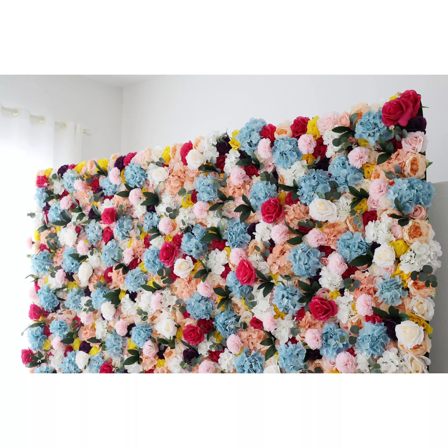 This is a large, vibrant artificial flower wall. It features a dense mix of colorful blooms—blue hydrangeas, pink roses, white flowers, and yellow blossoms. The lush arrangement creates a lively, eye - catching display, perfect for event backdrops, adding a cheerful and decorative touch to the space. 