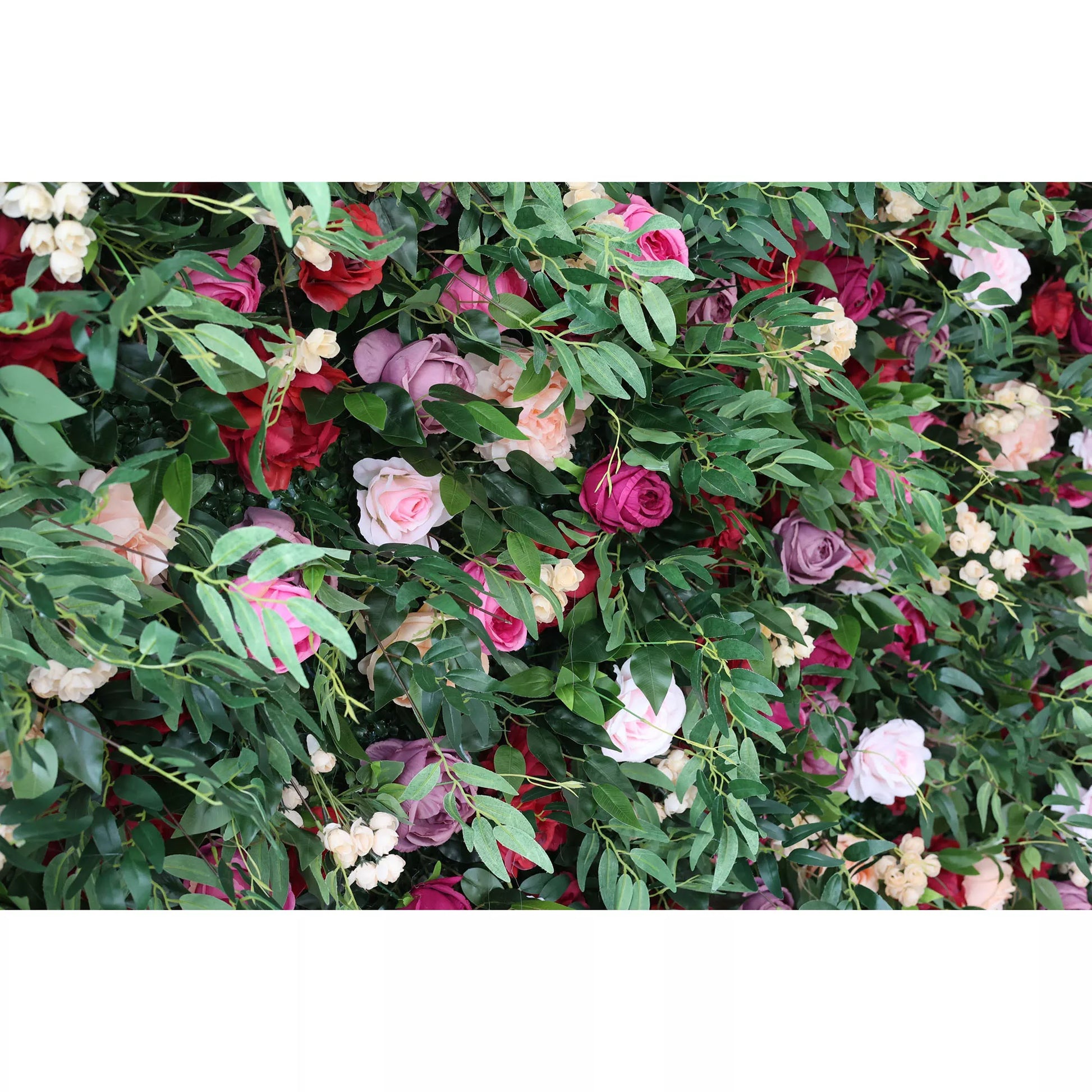 A close - up of an artificial flower wall features a vibrant mix of roses in pink, red, purple, and peach, interspersed with green foliage and small white blooms. The lush arrangement creates a romantic, decorative backdrop, ideal for events or adding a touch of elegance to a space. 