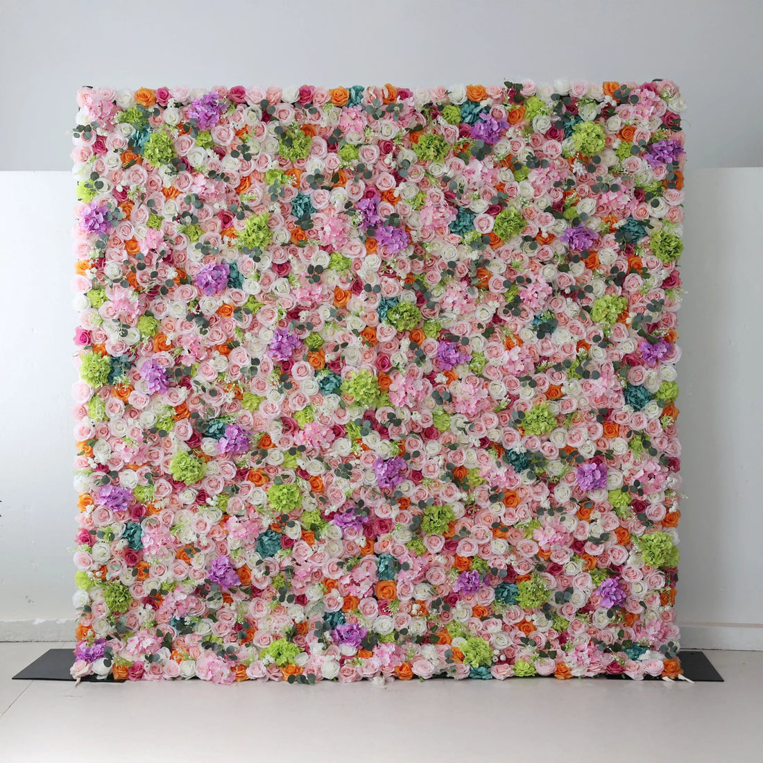This flower wall is a vibrant, dense display of artificial blooms. A harmonious mix of colors—white, pink, purple, orange, and green—creates a lively, celebratory feel. Varied flower types and textures add depth, making it perfect for events like weddings or parties, exuding joy and elegance. 