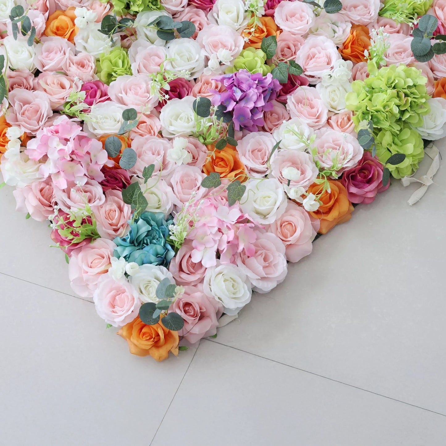 This is a close-up of a vibrant artificial floral arrangement from **Valar Flowers**, featuring a lush mix of soft pink, white, orange, deep red, purple, and turquoise blooms, complemented by green hydrangeas and eucalyptus leaves. Densely packed and layered, it creates a romantic, elegant aesthetic ideal for wedding decor, photo backdrops, or special event styling.