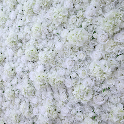 A dense arrangement of artificial white flowers forms a lush wall. It features various blooms like roses and hydrangeas, with subtle green leaves peeking through. The pure white hues create an elegant, romantic look, perfect for events such as weddings, bridal showers, or upscale parties needing a sophisticated backdrop.