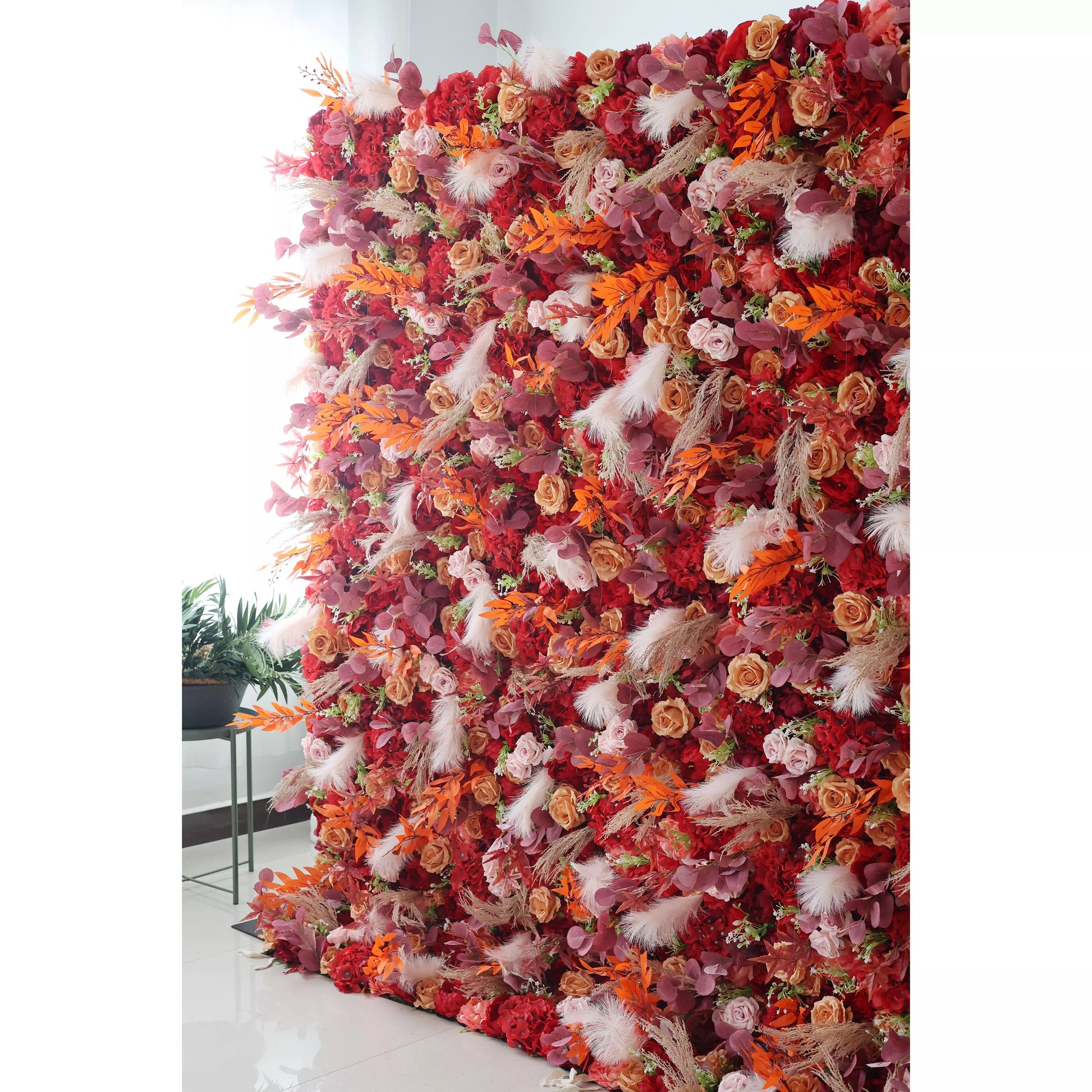 This flower wall is a spectacular arrangement, densely covered with artificial flowers. It features a warm and rich color scheme, blending deep reds, oranges, and soft pinks. Interspersed among the blooms are white feather - like decorations and various types of foliage, adding texture and a touch of whimsy. Ideal for weddings, parties, or other grand events, it serves as a striking and elegant backdrop, exuding a passionate and luxurious atmosphere. 