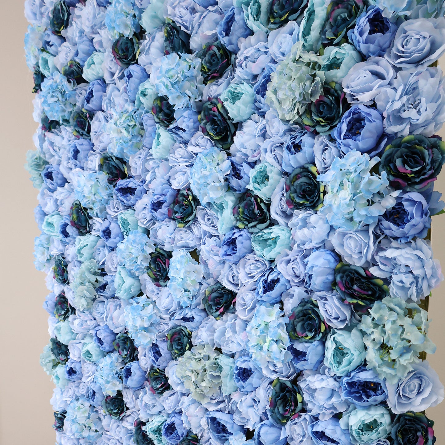 This image showcases a dense, lush arrangement of artificial flowers in various shades of blue—from light sky blue to deep navy. Featuring roses and hydrangeas, the textured display exudes elegance, ideal for a luxurious, nature-inspired backdrop by ValarFlowers, perfect for events or interiors.