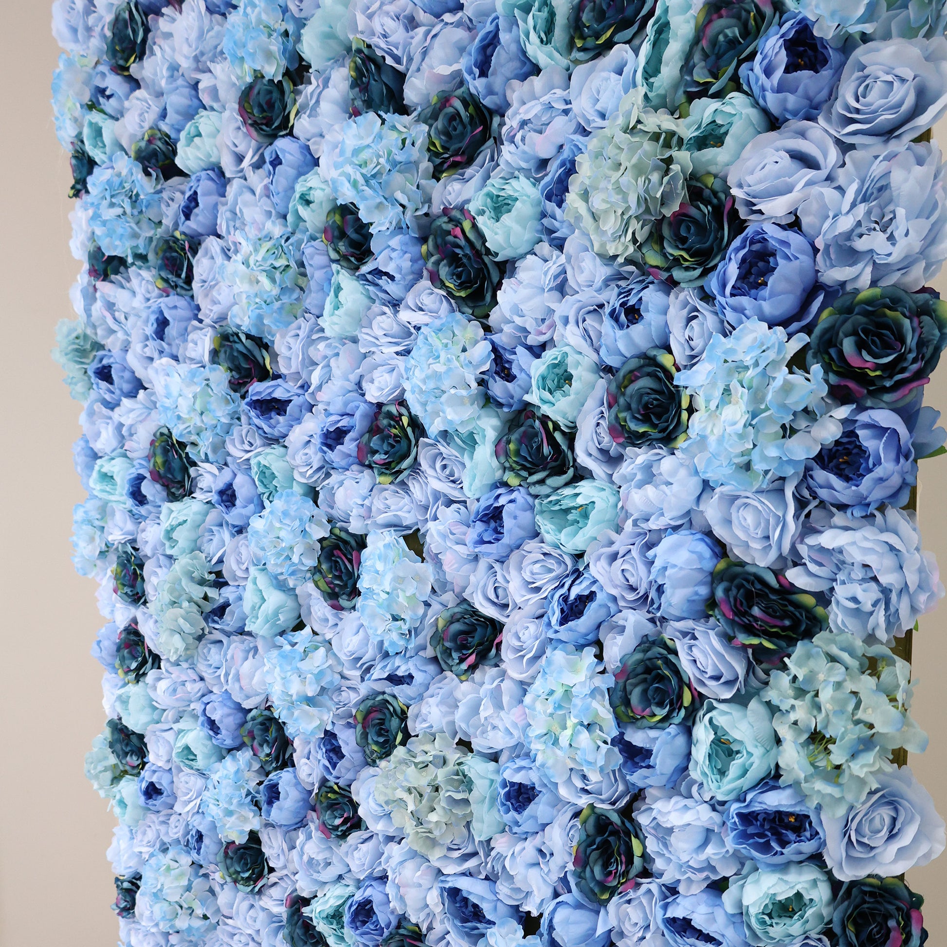 This image showcases a dense, lush arrangement of artificial flowers in various shades of blue—from light sky blue to deep navy. Featuring roses and hydrangeas, the textured display exudes elegance, ideal for a luxurious, nature-inspired backdrop by ValarFlowers, perfect for events or interiors.