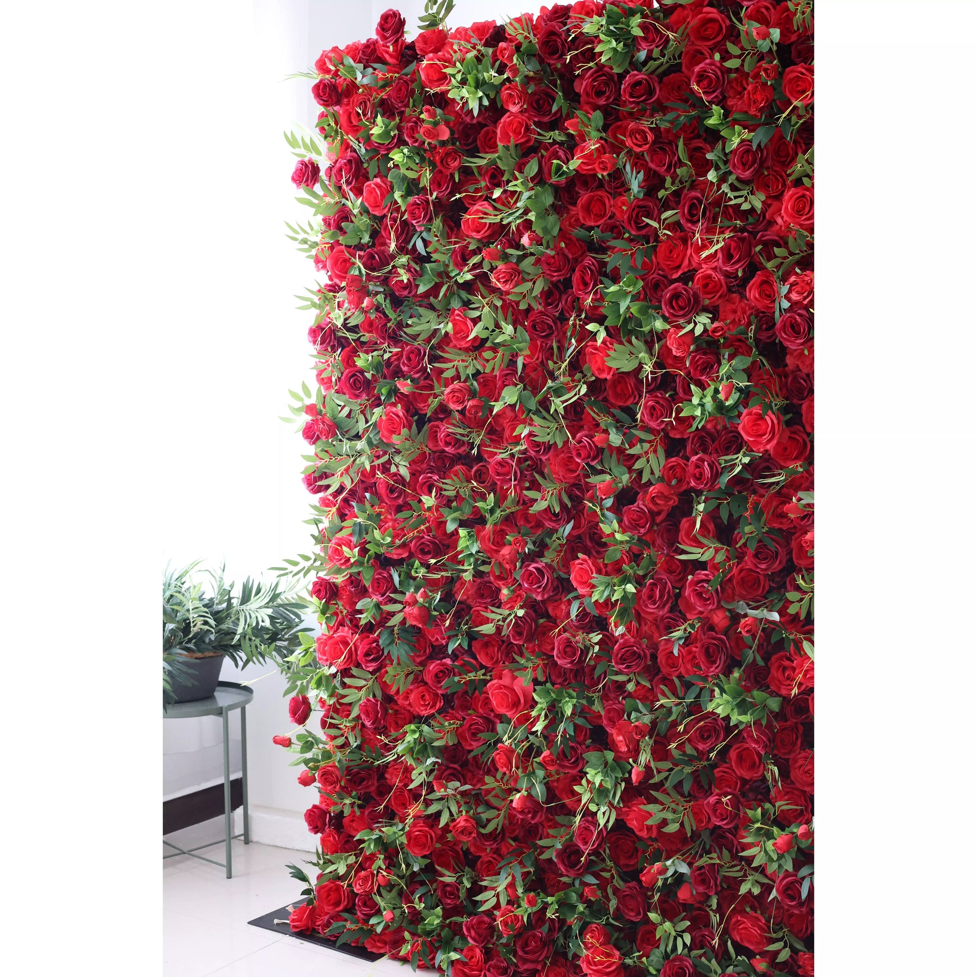This flower wall features a dense arrangement of artificial red roses, interspersed with lush green leaves. The deep red blooms create a passionate, romantic texture, while the foliage adds freshness. Perfect for weddings or events, it exudes elegance and intensity, serving as a striking backdrop for photos and decor. 
