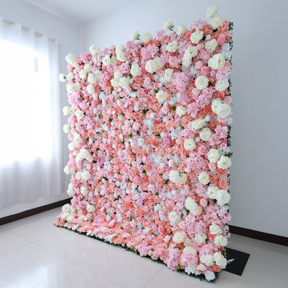 This image showcases a lush floral backdrop by ValarFlowers, set indoors. It features a dense arrangement of artificial flowers in shades of pink, peach, and white, creating a luxurious, textured display. Natural light from a window enhances the scene, exuding elegance and sophistication, perfect for adding a nature-inspired element to events or interiors.