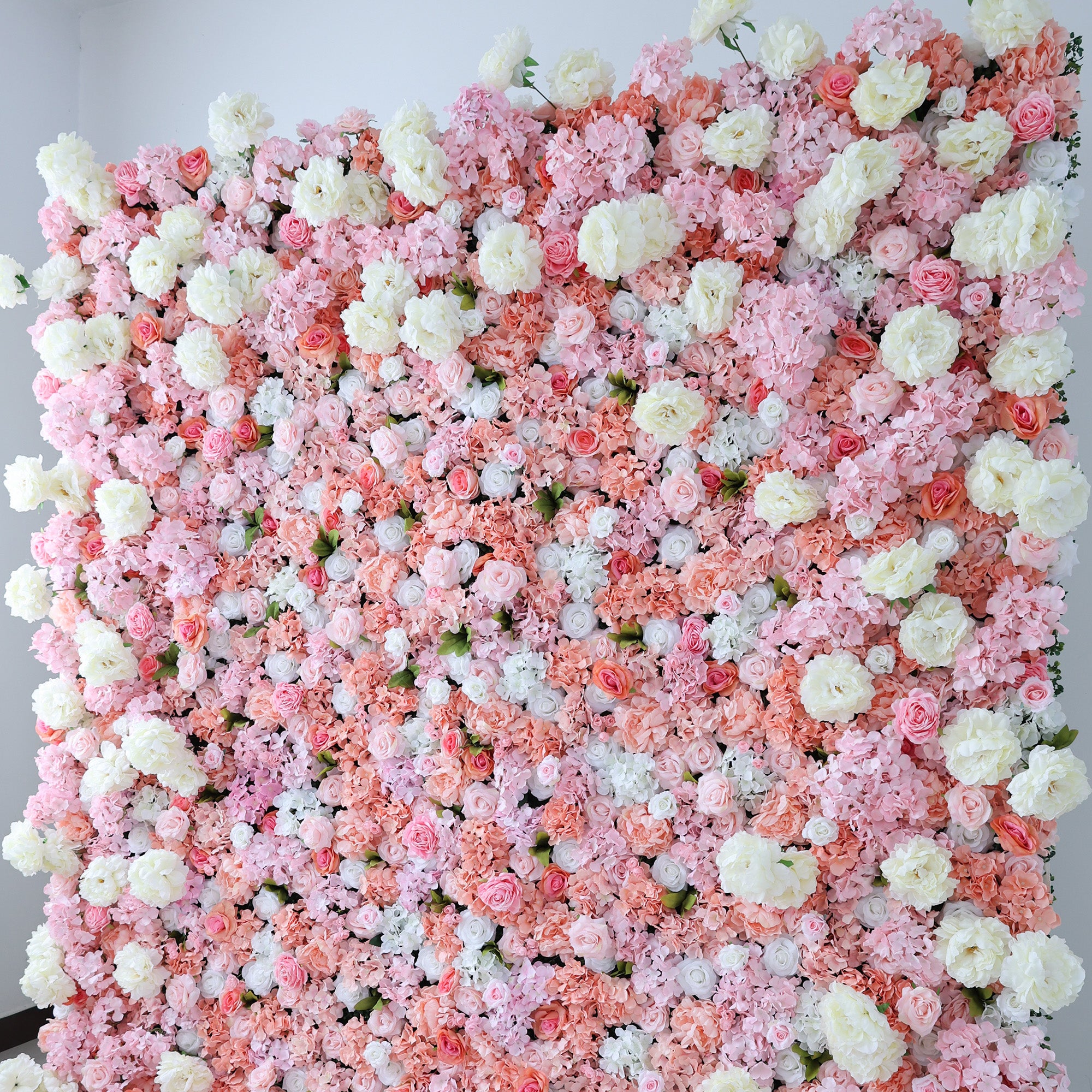 This image showcases a lush floral backdrop by ValarFlowers, featuring a dense arrangement of artificial flowers in shades of pink, peach, and white. The textured display exudes elegance, perfect for adding a luxurious, nature-inspired element to events or interiors, with its vibrant and sophisticated design.