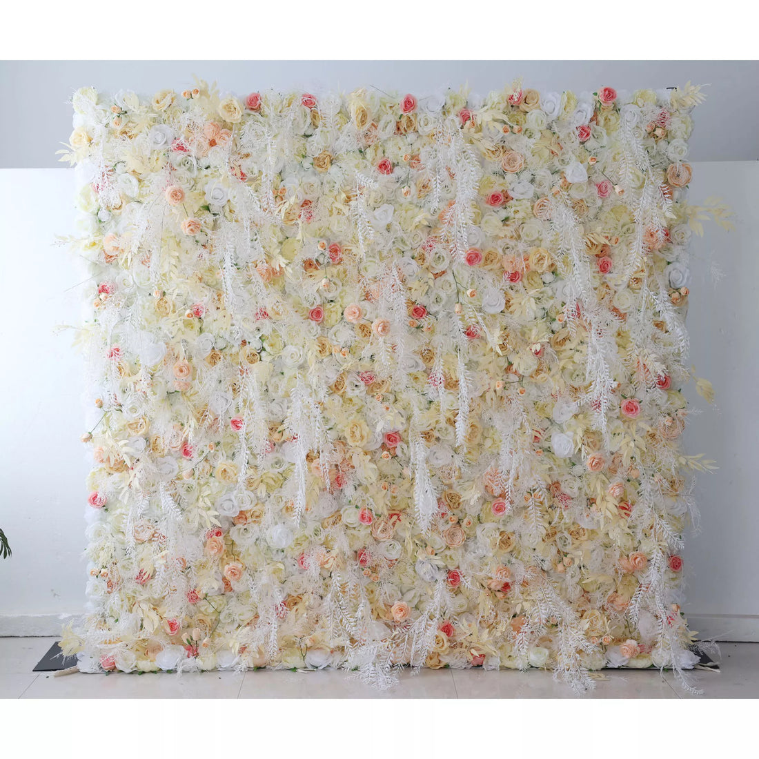 This flower wall is a delicate blend of cream, white, and soft pink artificial blooms. It features roses, tiny flowers, and feathery foliage, creating a light, airy texture. Subtle red accents add charm, making it perfect for weddings or elegant events. It exudes a romantic, ethereal vibe as a dreamy backdrop.