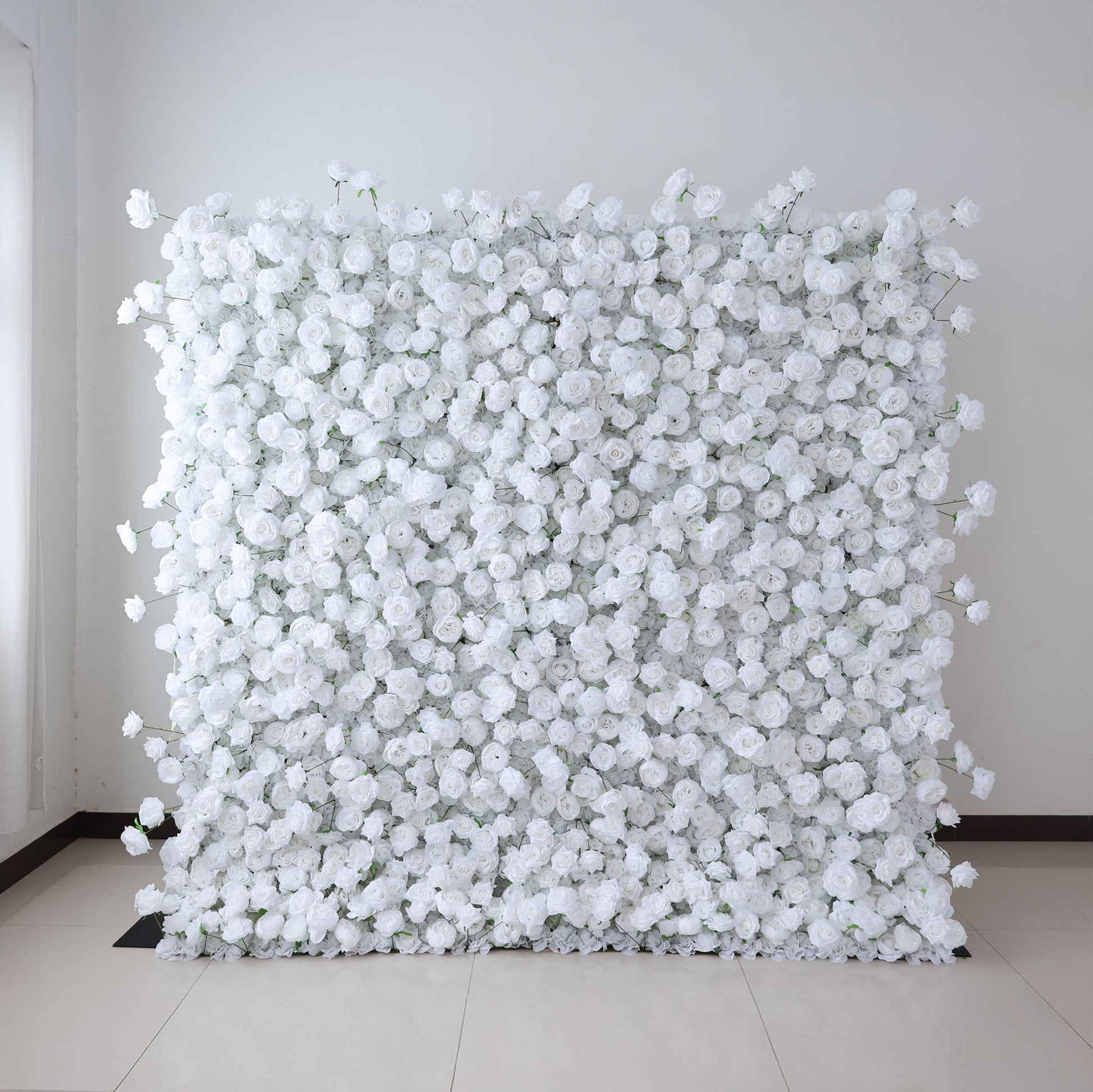 This image showcases a large, square floral wall indoors. It's densely covered with pure white artificial flowers, creating a clean, elegant, and serene display. The flowers are tightly packed, giving a sense of opulence and purity. Set against a plain white wall with a shiny tiled floor, the scene exudes an atmosphere of sophistication and natural beauty, perfect for decorative purposes in events or as a striking interior backdrop.