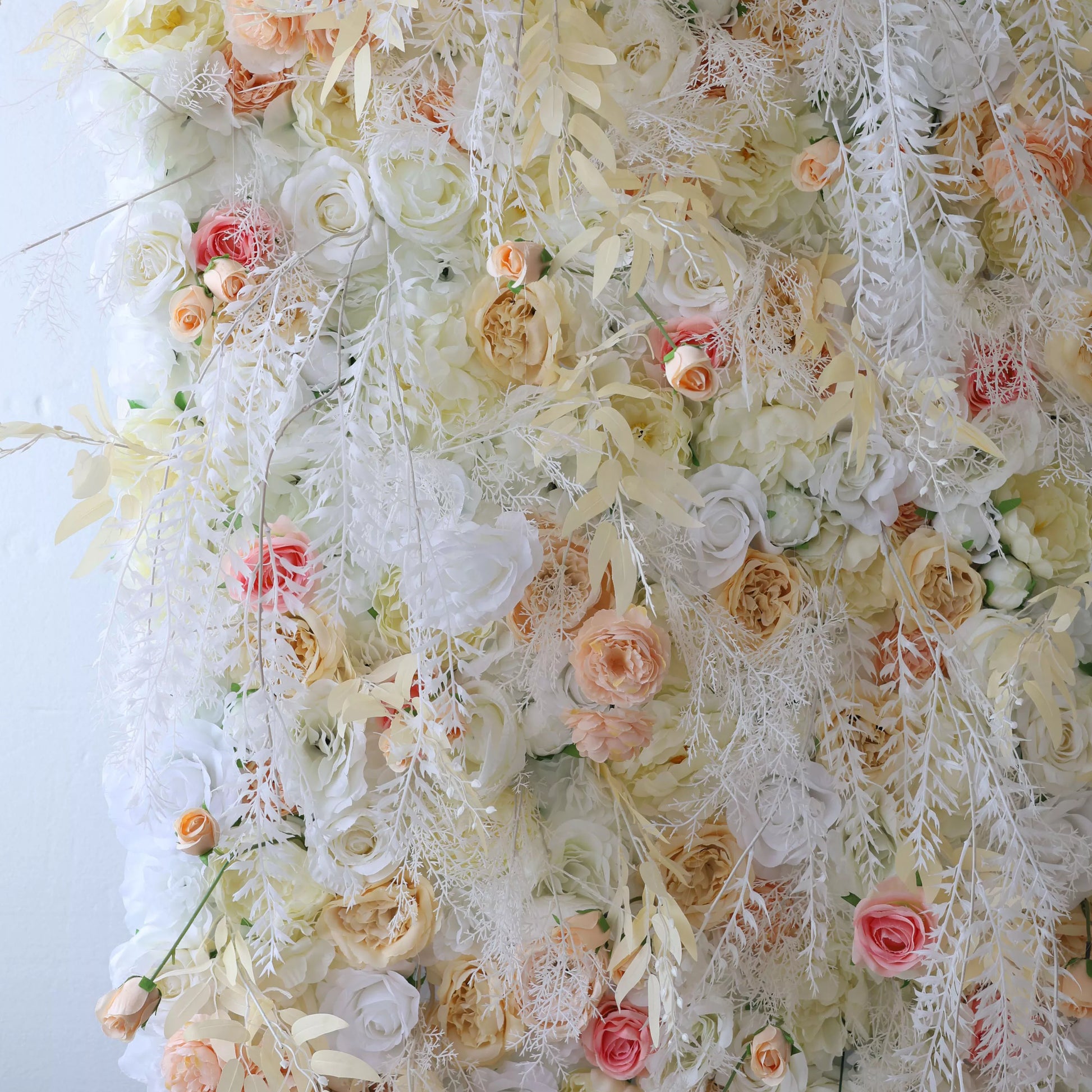 This flower wall is a beautiful blend of cream, white, and soft pink artificial blooms. It features roses, peonies, and delicate trailing vines, creating a lush, romantic texture. Subtle color gradients and feathery foliage add depth, making it perfect for weddings or elegant events, exuding an ethereal, dreamy charm. 