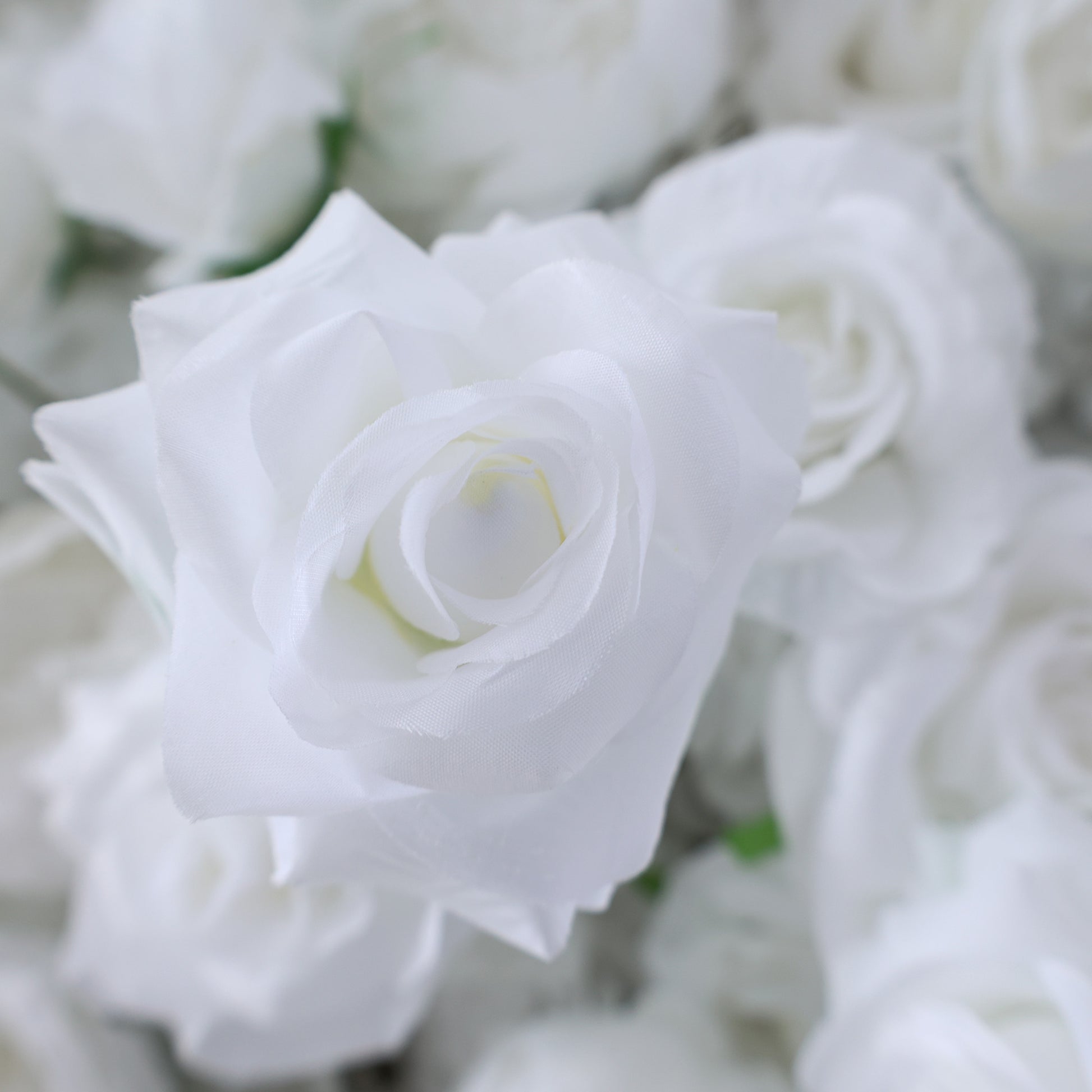 This picture features a close - up of a white artificial rose. The petals are soft and smooth, with a pristine white hue that gives a sense of purity. The rose's layers of petals are neatly arranged, creating a delicate and elegant appearance. Surrounding it are other similar white artificial roses, forming a lush cluster. The overall scene exudes a serene and sophisticated charm, ideal for decorative purposes in events or as part of a floral arrangement, evoking feelings of beauty and refinement.