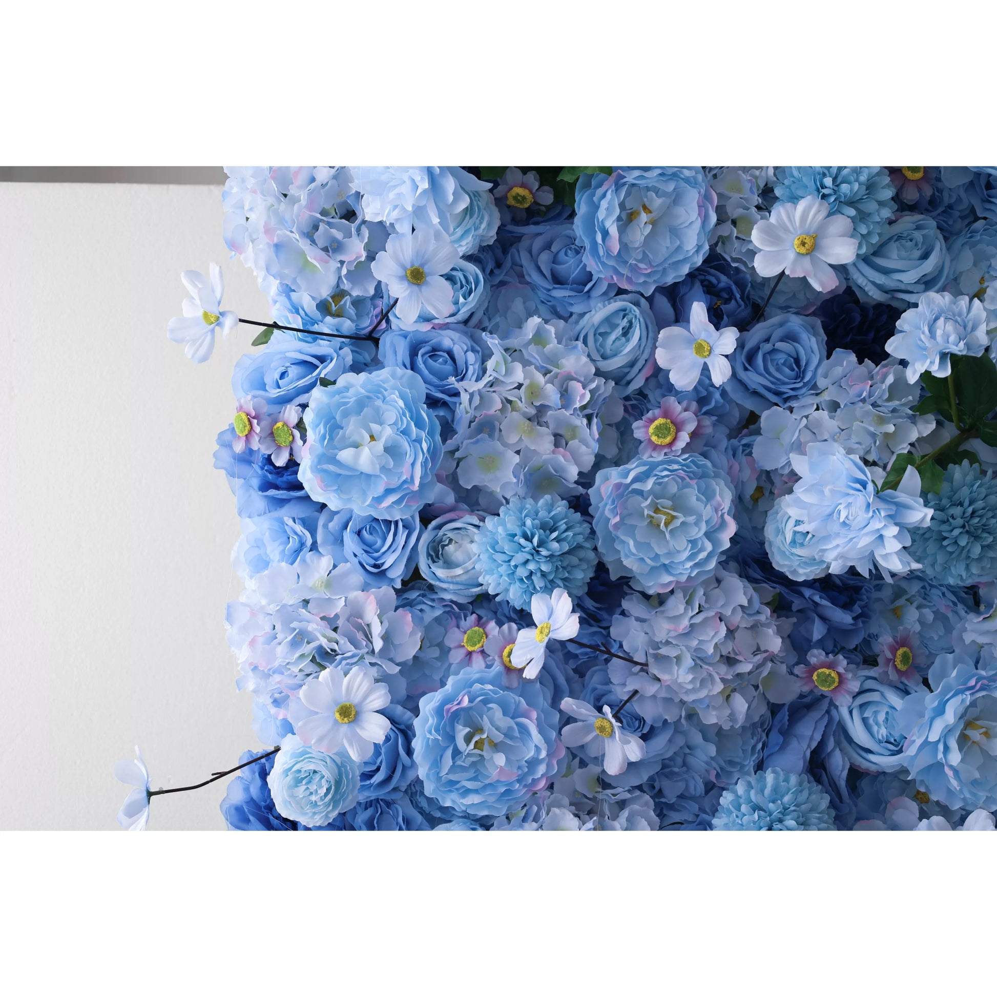 A close - up of an artificial flower wall showcases a harmonious blend of blue blooms. It includes soft - hued peonies, delicate daisies, and textured chrysanthemums, with subtle pink accents on some petals. The varied shapes and shades create a lush, elegant tapestry, perfect for adding a serene, decorative touch to spaces or events. 