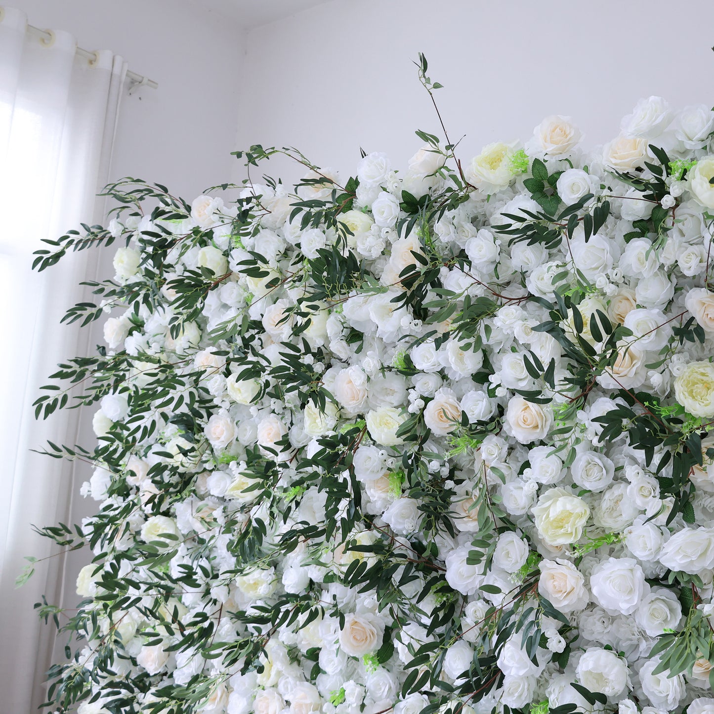 This image showcases a stunning floral arrangement by ValarFlowers. It features a dense cluster of artificial flowers in soft shades of white and cream, interspersed with lush green foliage. The meticulously crafted blooms, including roses and other complementary flowers, create a lush, elegant, and visually soothing display. 