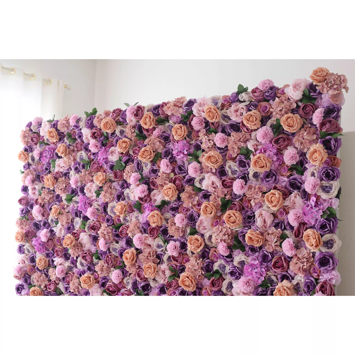 This flower wall is a lush, vibrant display of artificial blooms. A harmonious blend of purple, lavender, and peach roses, plus delicate pink flowers, creates a dreamy, romantic texture. The dense arrangement and soft color palette make it perfect for weddings or elegant events, exuding charm and elegance. 