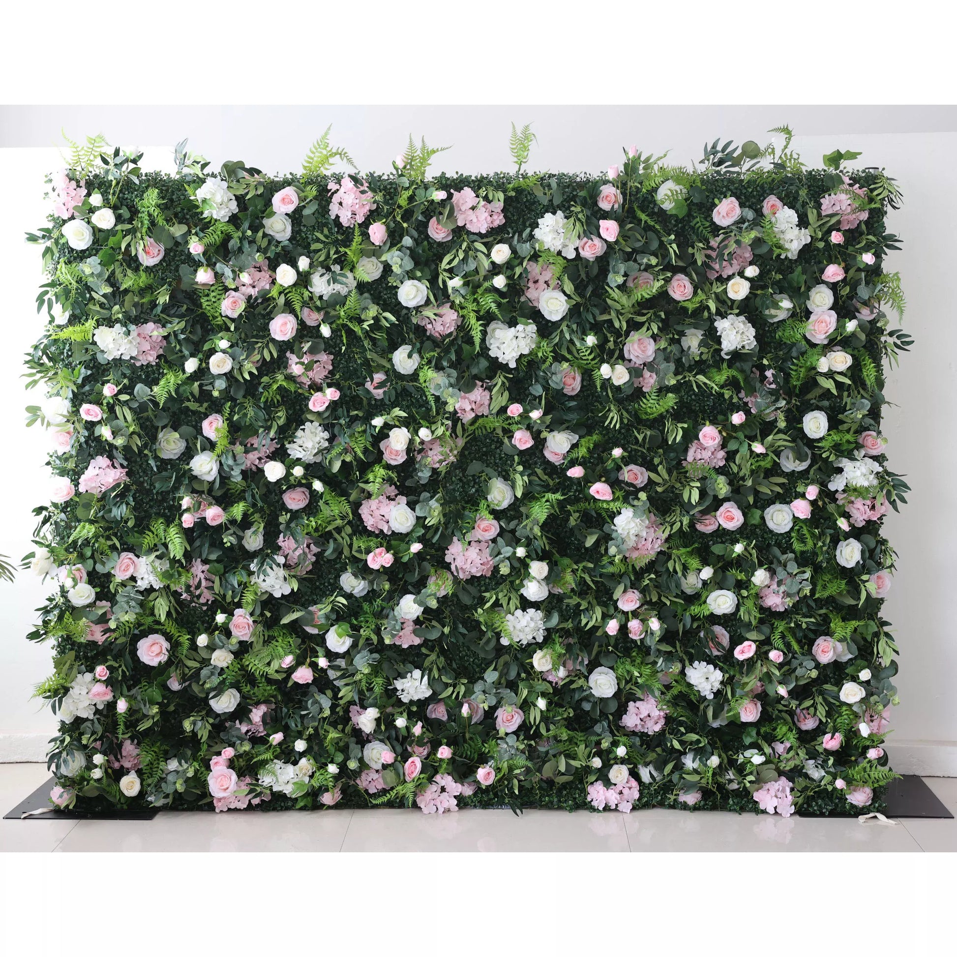 This lush floral wall features a dense, textured backdrop of deep green foliage, interspersed with a romantic mix of blush pink, soft white, and pale pink blooms—including roses, hydrangeas, and delicate filler flowers. The layered design creates a rich, three-dimensional texture, evoking a fresh, natural, and romantic atmosphere ideal for weddings, photo backdrops, or elegant celebrations.