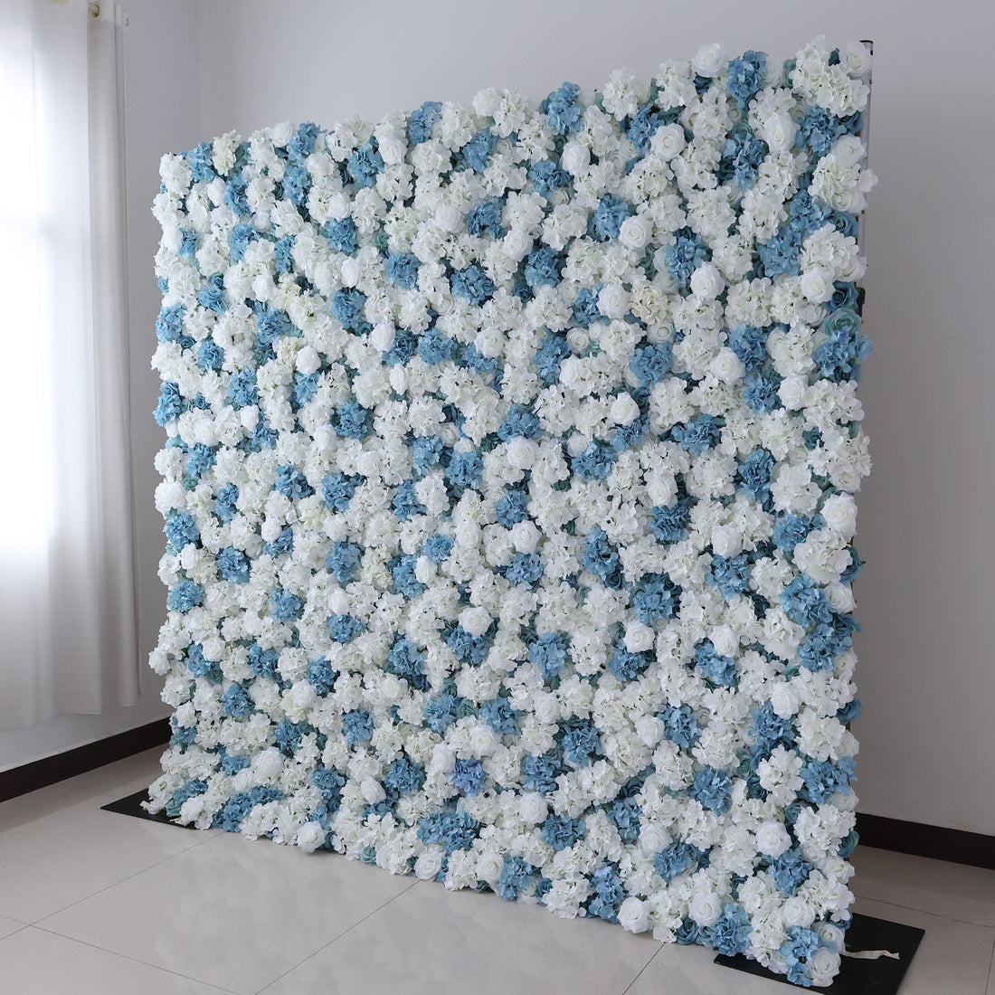 A large, square floral wall showcases a beautiful blend of white and blue artificial flowers. Dense clusters of blooms create a lush, elegant display. Set in a room with light - colored walls, a tiled floor, and a window with sheer curtains letting in soft light, it exudes a fresh and sophisticated vibe, perfect for events like weddings, parties, or as a decorative photo backdrop.