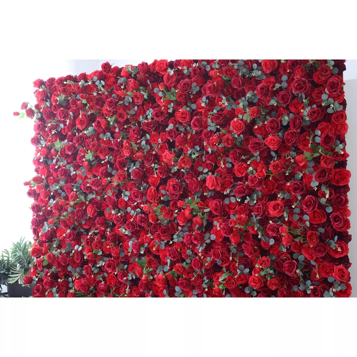 This flower wall is a lavish display of artificial red roses interspersed with green leaves. The dense, uniform arrangement creates a rich, passionate texture. Perfect for events needing a dramatic, romantic backdrop, exuding elegance and intensity. A striking centerpiece for weddings or celebrations. 