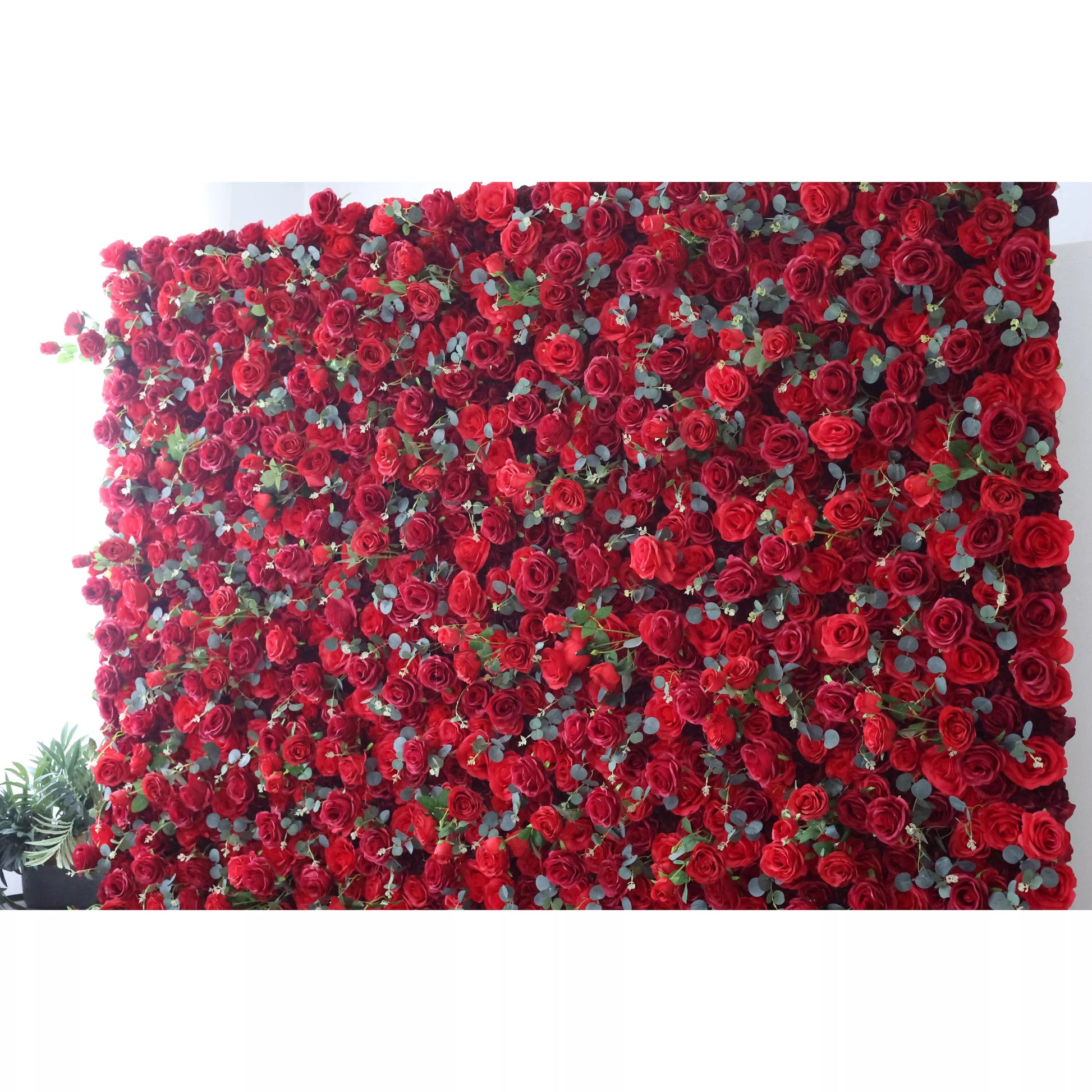 This flower wall is a lavish display of artificial red roses interspersed with green leaves. The dense, uniform arrangement creates a rich, passionate texture. Perfect for events needing a dramatic, romantic backdrop, exuding elegance and intensity. A striking centerpiece for weddings or celebrations. 