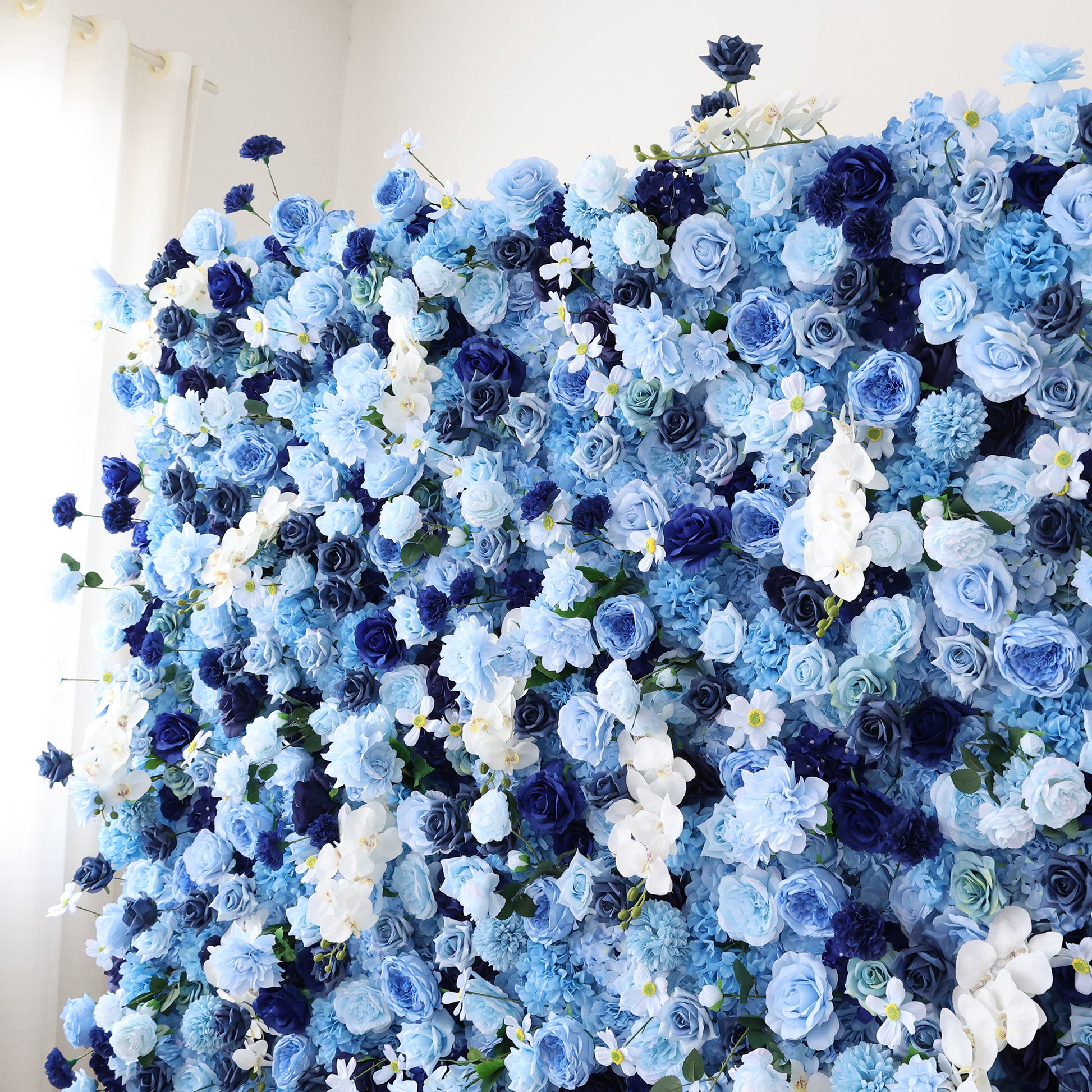 This close - up image showcases a dense arrangement of artificial flowers in various shades of blue and white. The flowers, including roses and other blooms, are clustered tightly to form a lush, elegant floral display. The harmonious blend of colors and intricate petals create a serene and refined scene, ideal for decorative purposes in events or as a visually appealing artistic display.