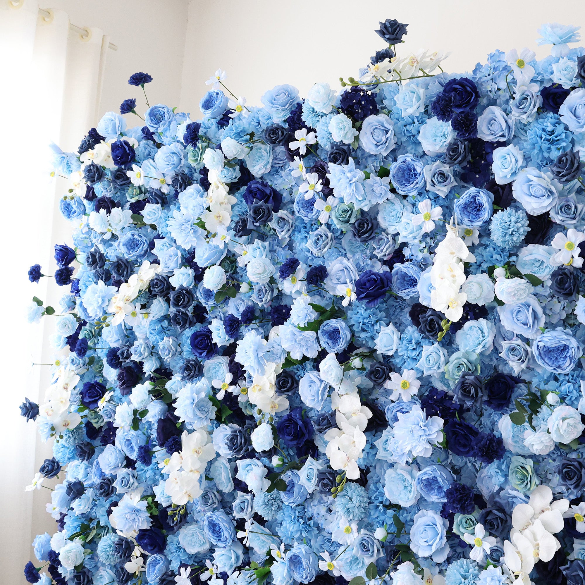 This close - up image showcases a dense arrangement of artificial flowers in various shades of blue and white. The flowers, including roses and other blooms, are clustered tightly to form a lush, elegant floral display. The harmonious blend of colors and intricate petals create a serene and refined scene, ideal for decorative purposes in events or as a visually appealing artistic display.