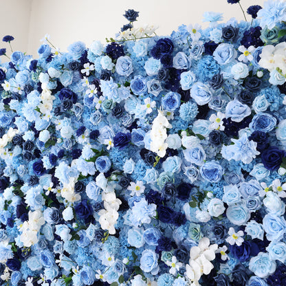 This image displays a dense, vibrant arrangement of artificial flowers in various shades of blue and white. The flowers, including roses and other blooms, are clustered tightly to form a lush, elegant floral display. The harmonious blend of colors and intricate petals create a serene and refined scene, ideal for decorative purposes in events or as a visually appealing artistic display.