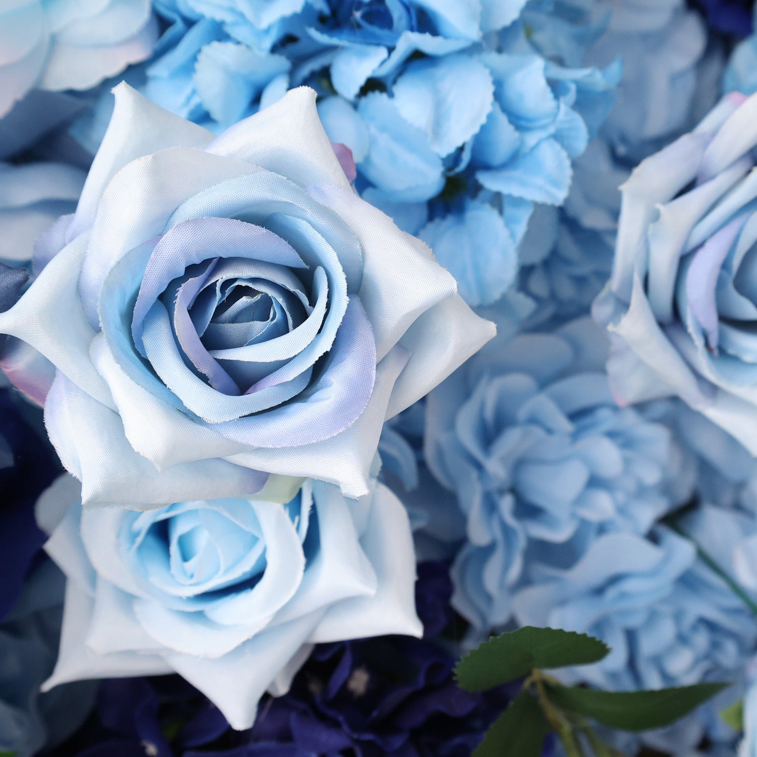 This close - up image showcases artificial light blue roses. The petals have a soft, satin - like texture with subtle color gradients, creating a delicate and realistic appearance. Surrounding the roses are other light blue floral elements, forming a cohesive and elegant arrangement. The overall scene exudes a sense of tranquility and refined beauty, ideal for decorative purposes in events or as a visually appealing artistic display.