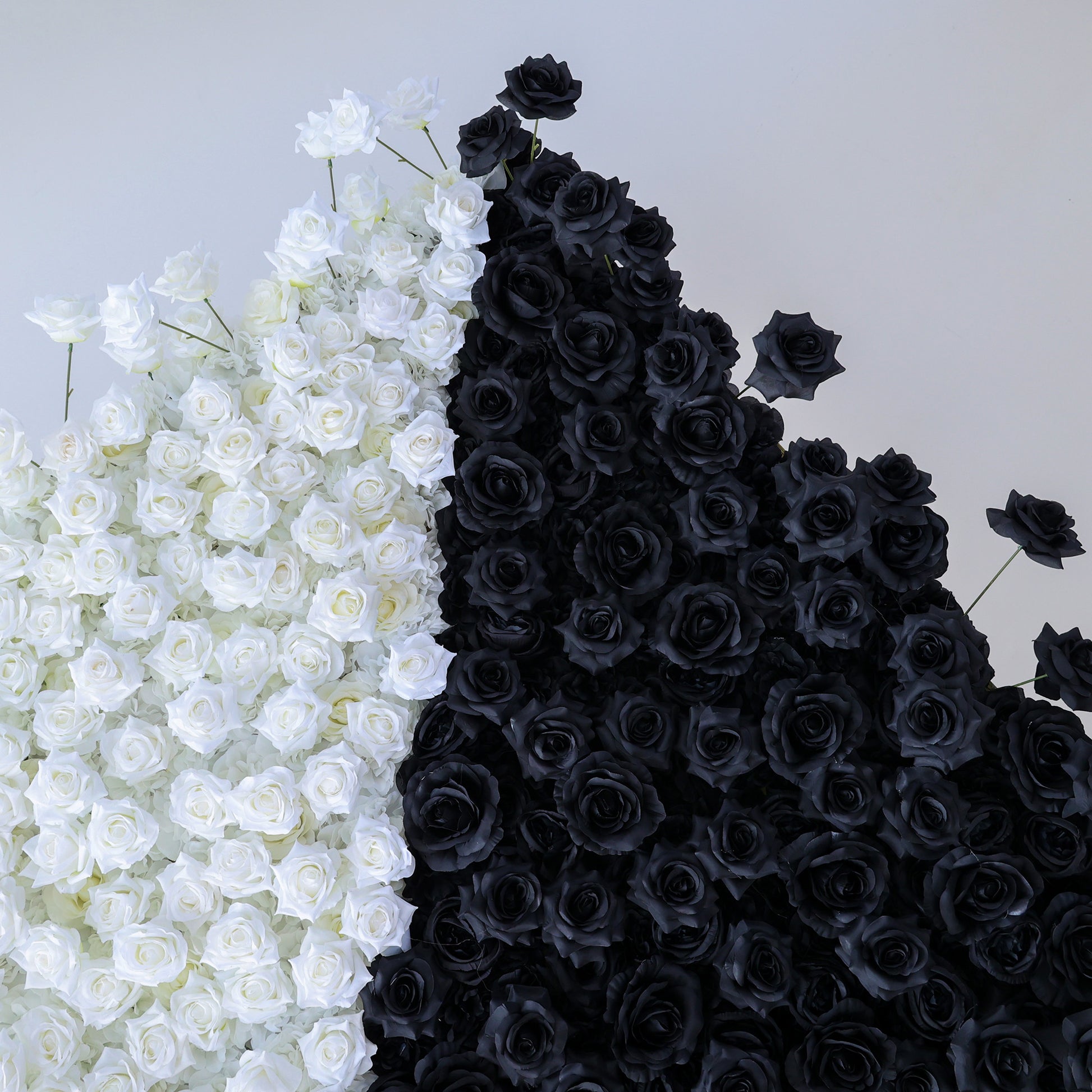 This photo presents a stunning floral wall by ValarFlowers, crafted from artificial roses. It's split diagonally into white and black sections, creating a bold, modern contrast. The uniform texture of the faux roses offers a polished, long-lasting display. Set against a clean, minimalist backdrop, this design makes a dramatic statement. Ideal for avant-garde events, fashion shows, or contemporary decor.