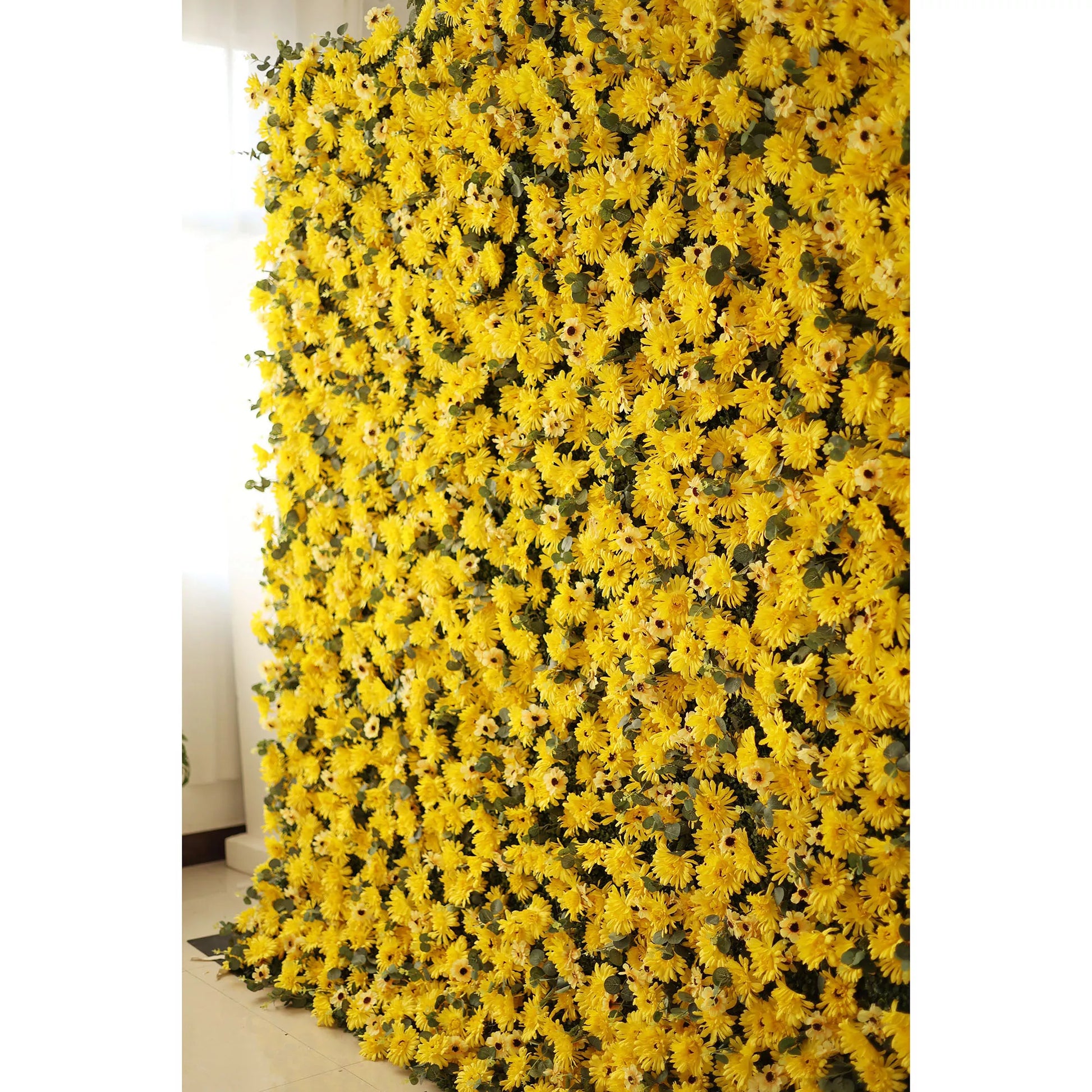 This vibrant indoor backdrop features a dense, textured arrangement of artificial yellow daisies with dark centers, layered with subtle green foliage. The bold, sun-drenched palette creates a cheerful, energy-filled effect that exudes warmth and joy. Set against a minimalist white wall and light floor, it serves as a lively focal point for summer events, photoshoots, or spaces seeking a bright, uplifting aesthetic.
