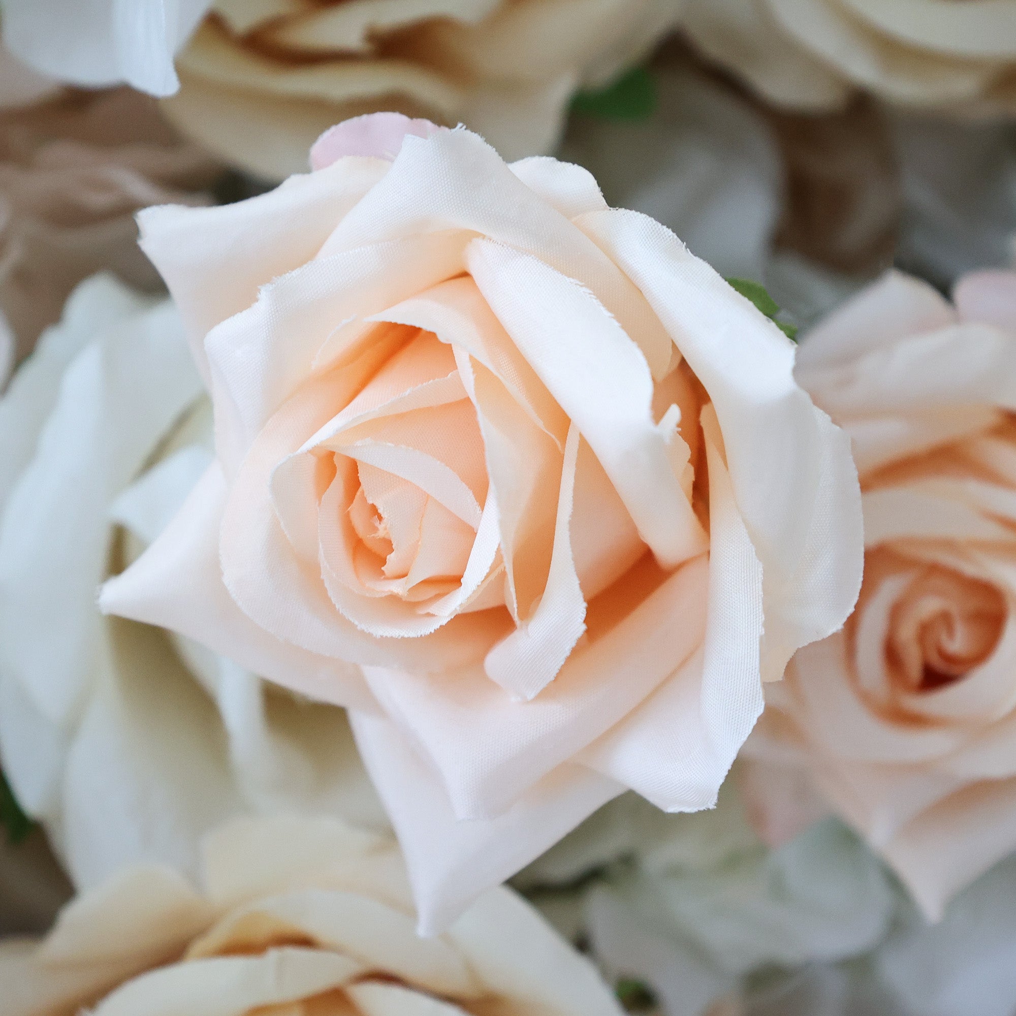 This close - up image showcases a single artificial peach - colored rose. The flower has numerous delicate, layered petals with a soft, slightly textured surface that mimics the look of real rose petals. The gradient from a lighter hue at the edges to a deeper peach in the center adds depth and realism to the bloom. Surrounding the rose are hints of other light - colored floral elements, creating a harmonious and elegant arrangement. The overall scene exudes a sense of grace and beauty, perfect for decorati