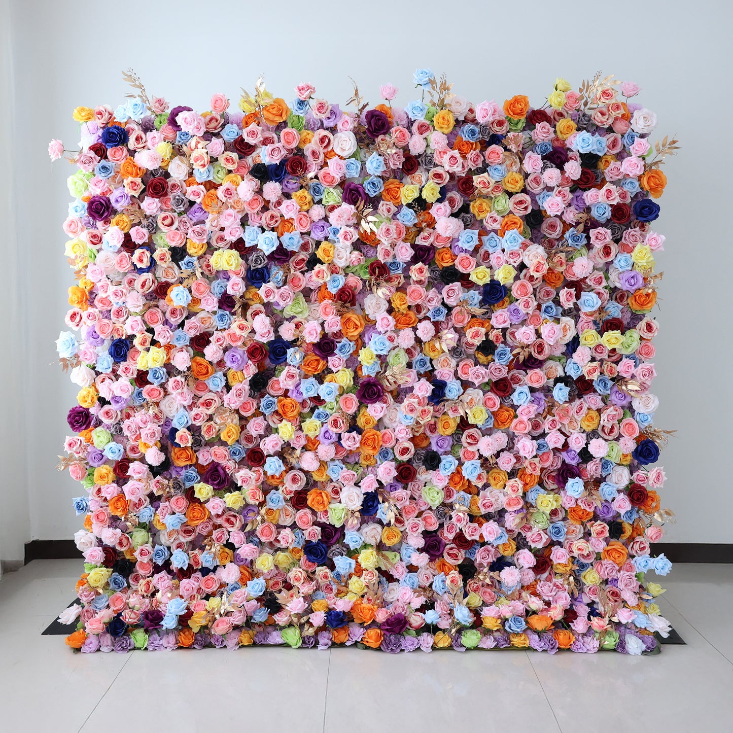 This image showcases a large, dense floral wall indoors. It's covered with an array of vibrant flowers in a wide spectrum of colors, including pink, purple, blue, orange, and yellow, creating a lively and eye - catching display. Set against a plain wall with a tiled floor, the scene exudes a sense of vibrancy and charm, perfect for decorative purposes in events or as a striking interior backdrop.