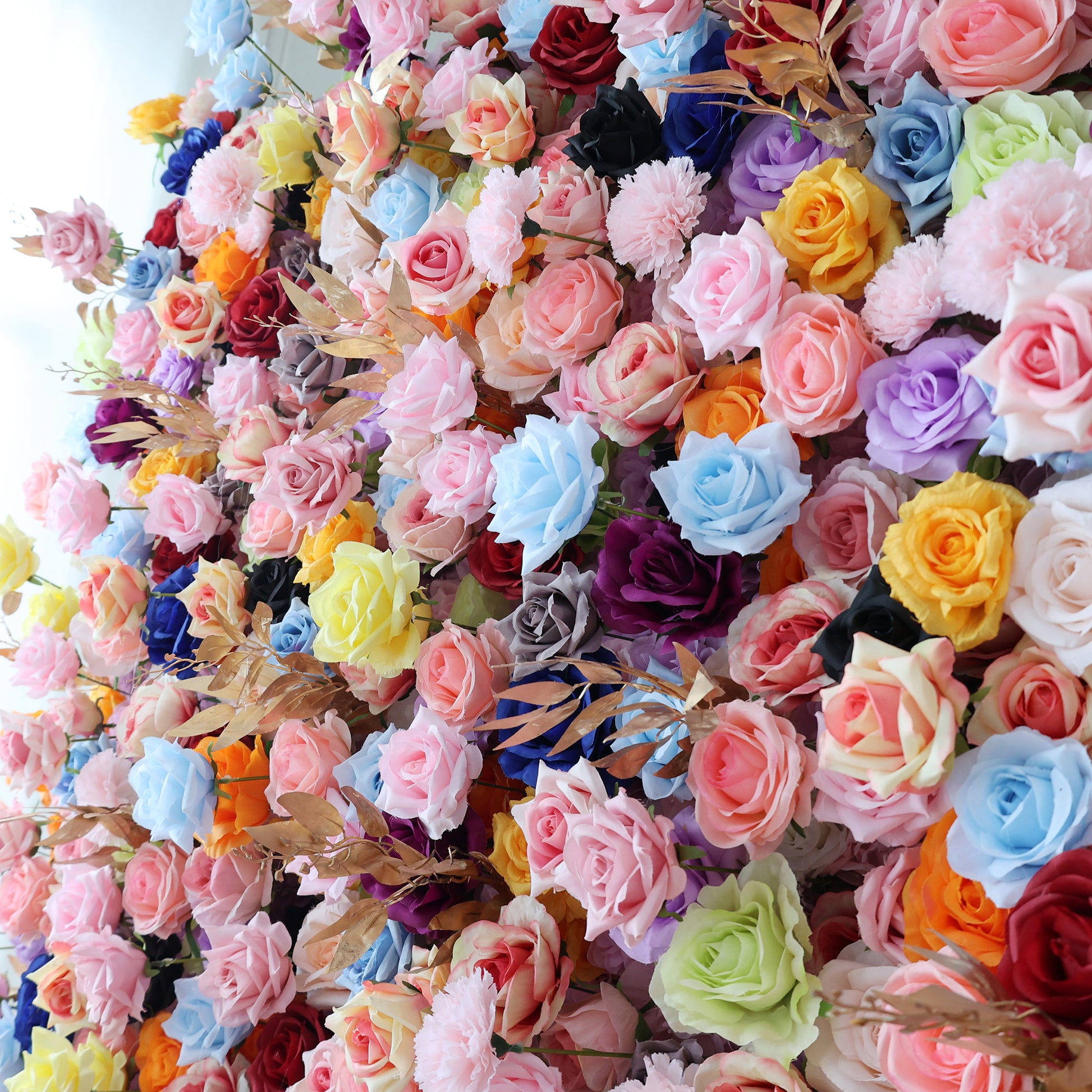 This close - up image showcases a dense arrangement of artificial flowers in a vibrant spectrum of colors. It features roses in shades like pink, blue, yellow, purple, orange, and more, along with other blooms. Interspersed are golden - hued foliage, creating a lush, colorful, and visually striking display, ideal for decorative purposes in events or as an attractive floral installation.