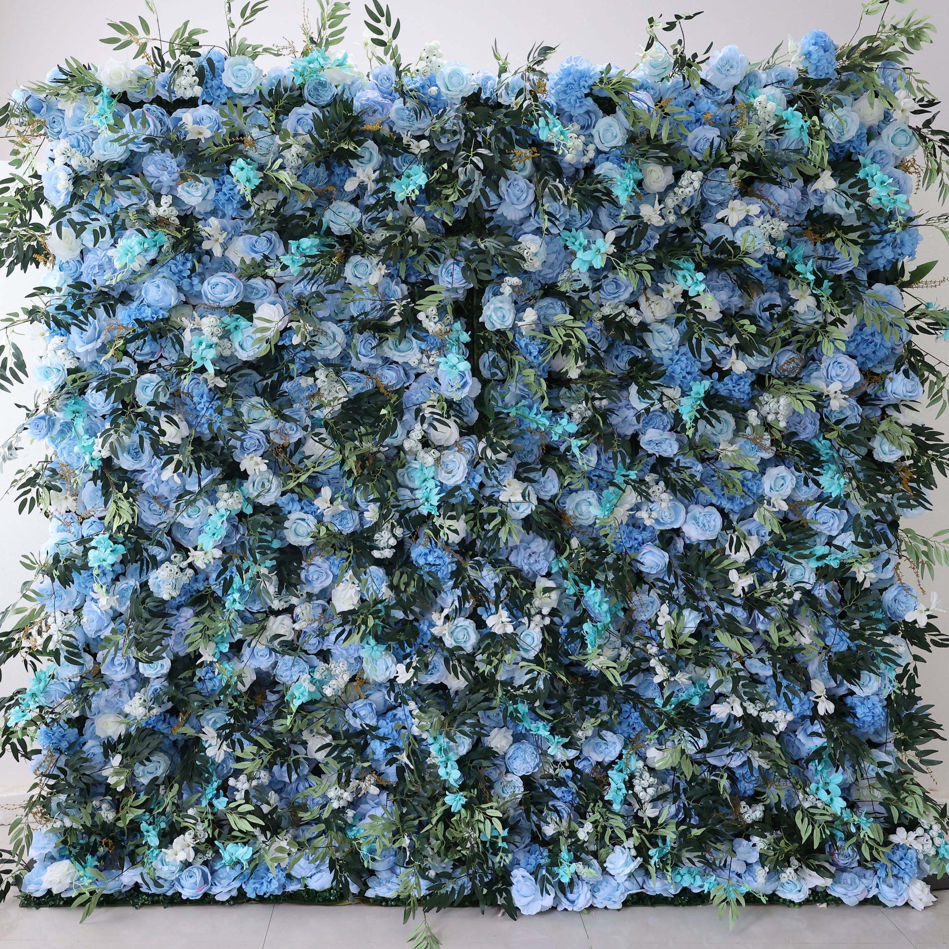 This image showcases a stunning floral wall by Valar Flowers. It features a dense arrangement of artificial flowers in various shades of blue, from light sky blue to deeper hues, complemented by white blooms. Lush green foliage is interspersed, creating a lush, serene, and visually captivating display. Perfect for adding an elegant, nature - inspired touch to events or interior spaces, it exudes a sense of tranquility and beauty.