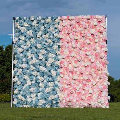 An outdoor floral wall on a metal frame divides into two sections. One side features blue and white artificial flowers, while the other has pink and white ones, set against a grassy area with a sky backdrop. 