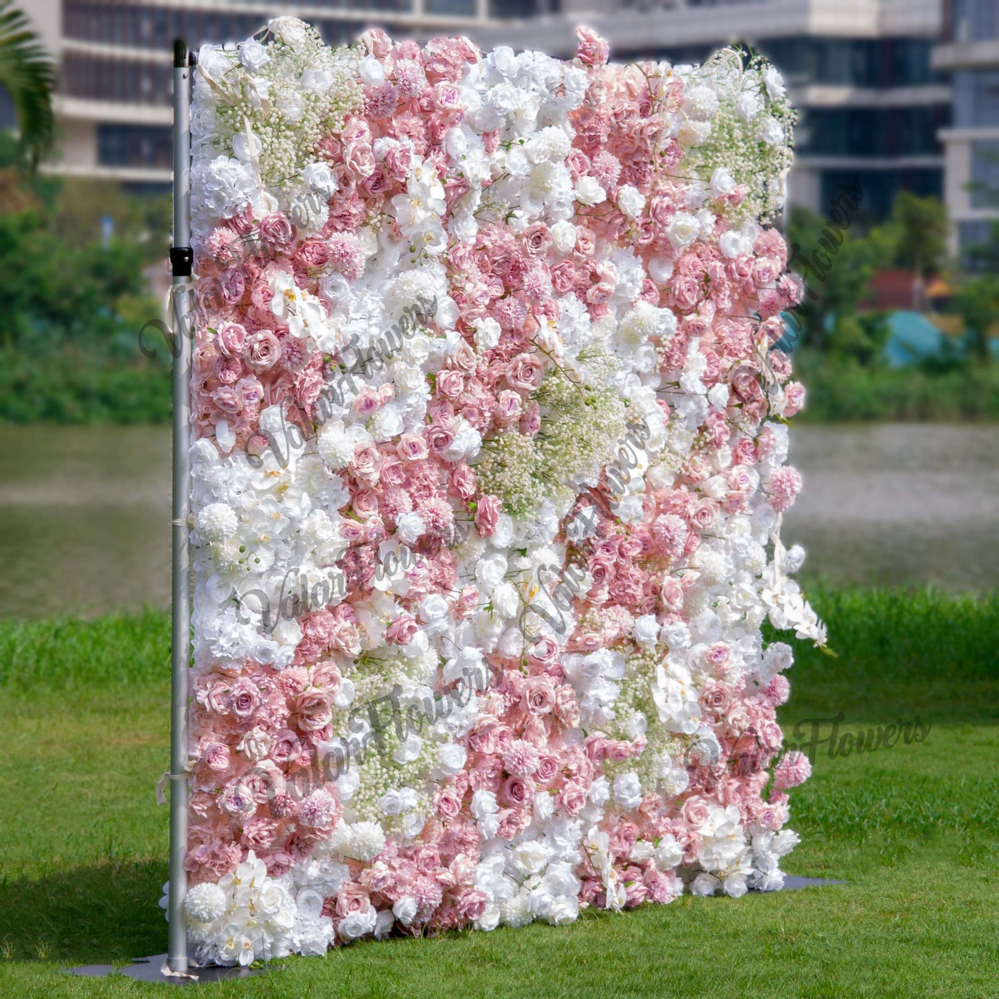 This backdrop is a vibrant floral wall supported by a metal frame. It features a mix of artificial flowers, including roses in soft pinks and whites, white hydrangeas, and clusters of baby's breath. The color palette is pastel - heavy, with gentle pinks and pure whites, creating a romantic and elegant style, perfect for wedding or event settings. 