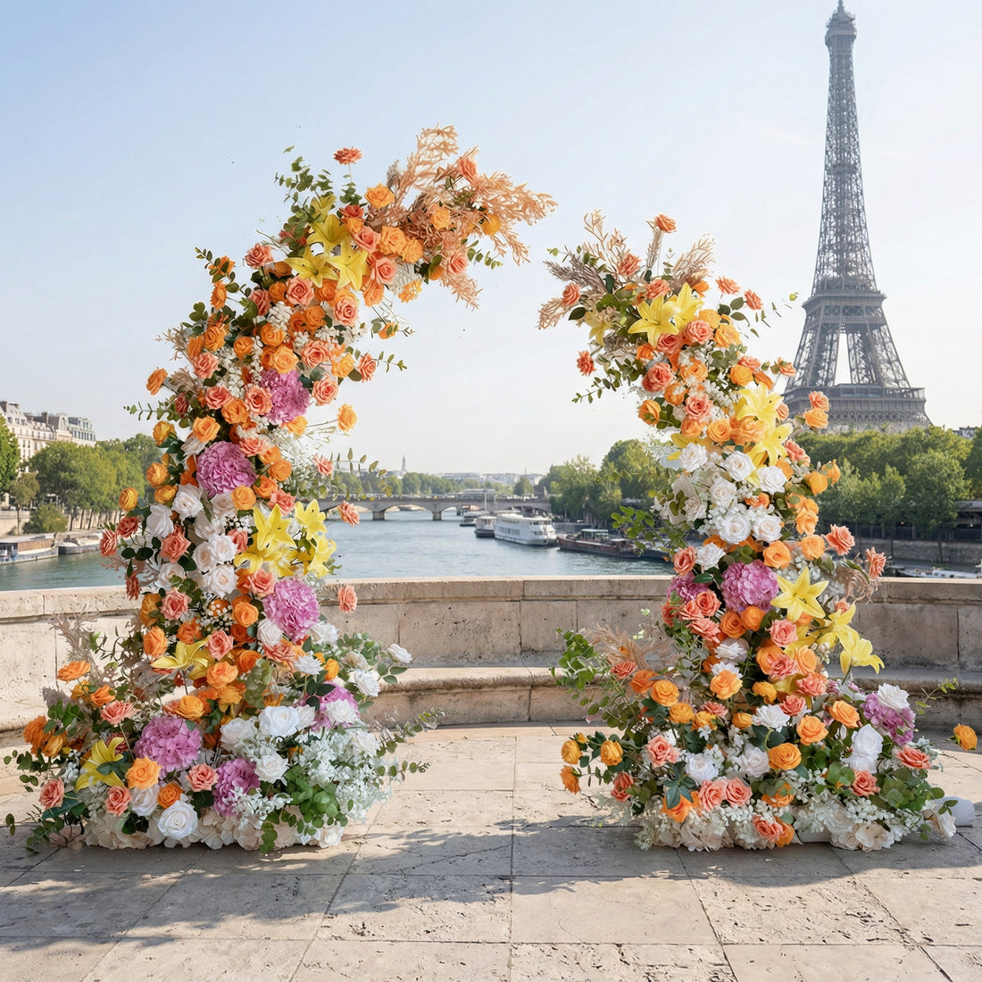A vibrant asymmetrical floral arch from Valar Flowers, ablaze with warm oranges, sunny yellows, pinks, and white blooms, accented with textured foliage. Set on a sun-drenched Parisian terrace with the Eiffel Tower backdrop, it exudes joyful, bold elegance—perfect for vibrant weddings and editorial shoots.