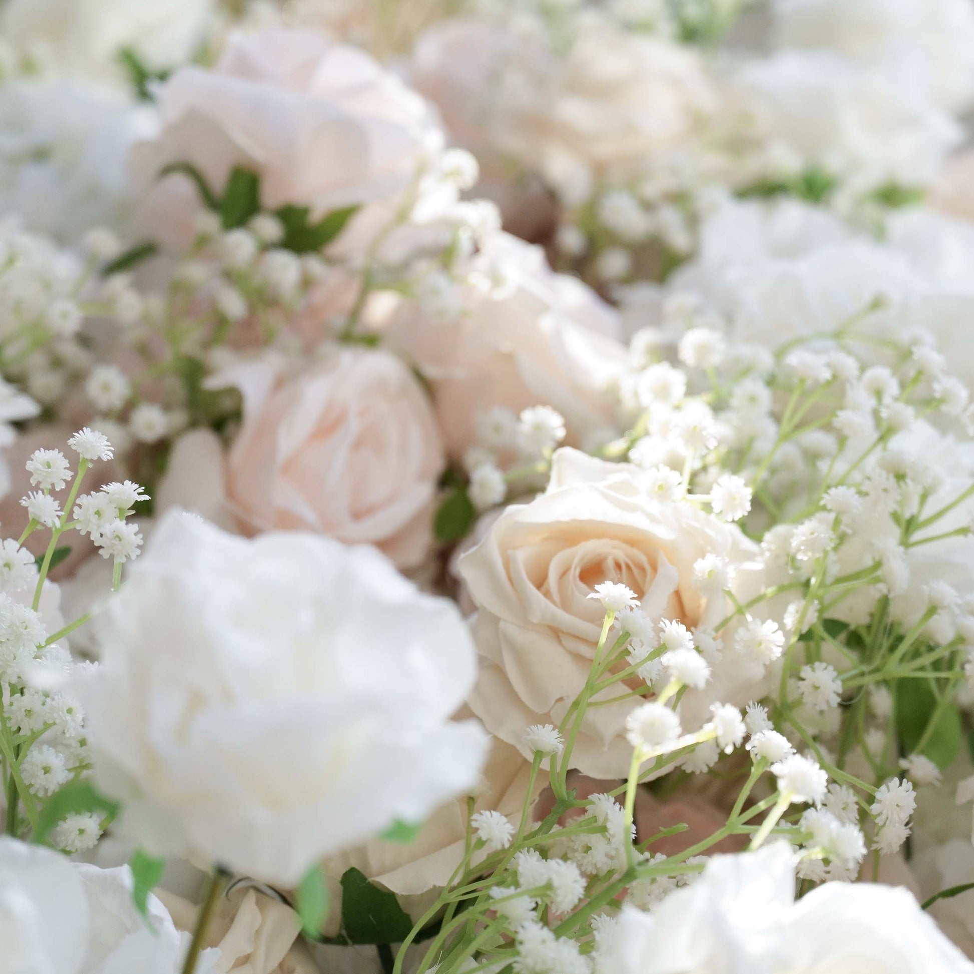 This close - up showcases a lush arrangement of artificial flowers. Prominently featured are roses in soft, pastel hues like light pink, cream, and white, interspersed with delicate sprigs of baby's - breath - like greenery. The color palette is gentle and soothing, exuding a romantic and elegant style, ideal for wedding or event backdrops. 