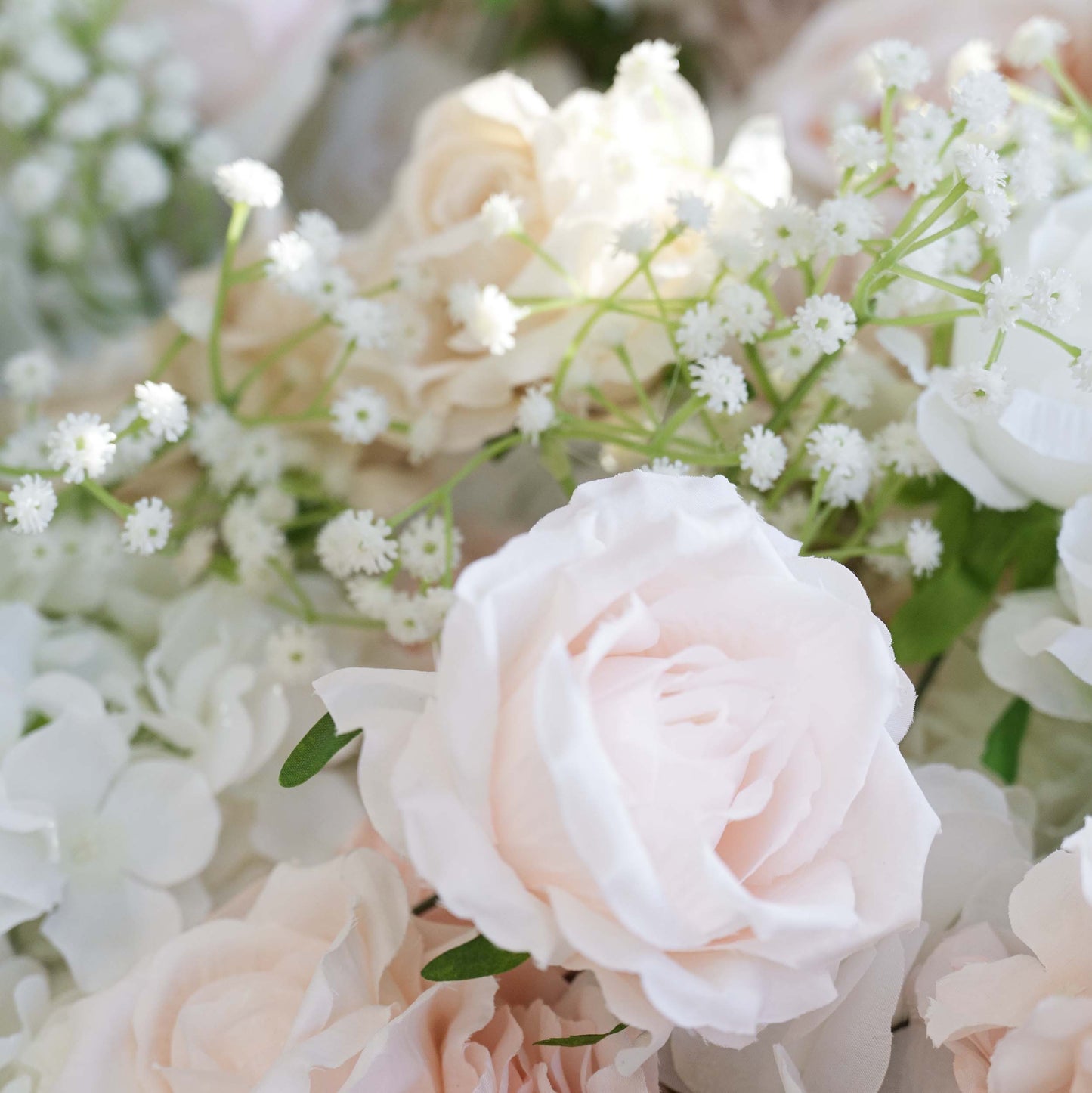 This close - up showcases elements of a floral backdrop. The main flowers are artificial roses in soft, pastel shades like light pink and cream, interspersed with delicate sprigs of baby's - breath - like greenery. The color palette is gentle and soothing, creating a romantic and elegant style, ideal for wedding or event decorations. 