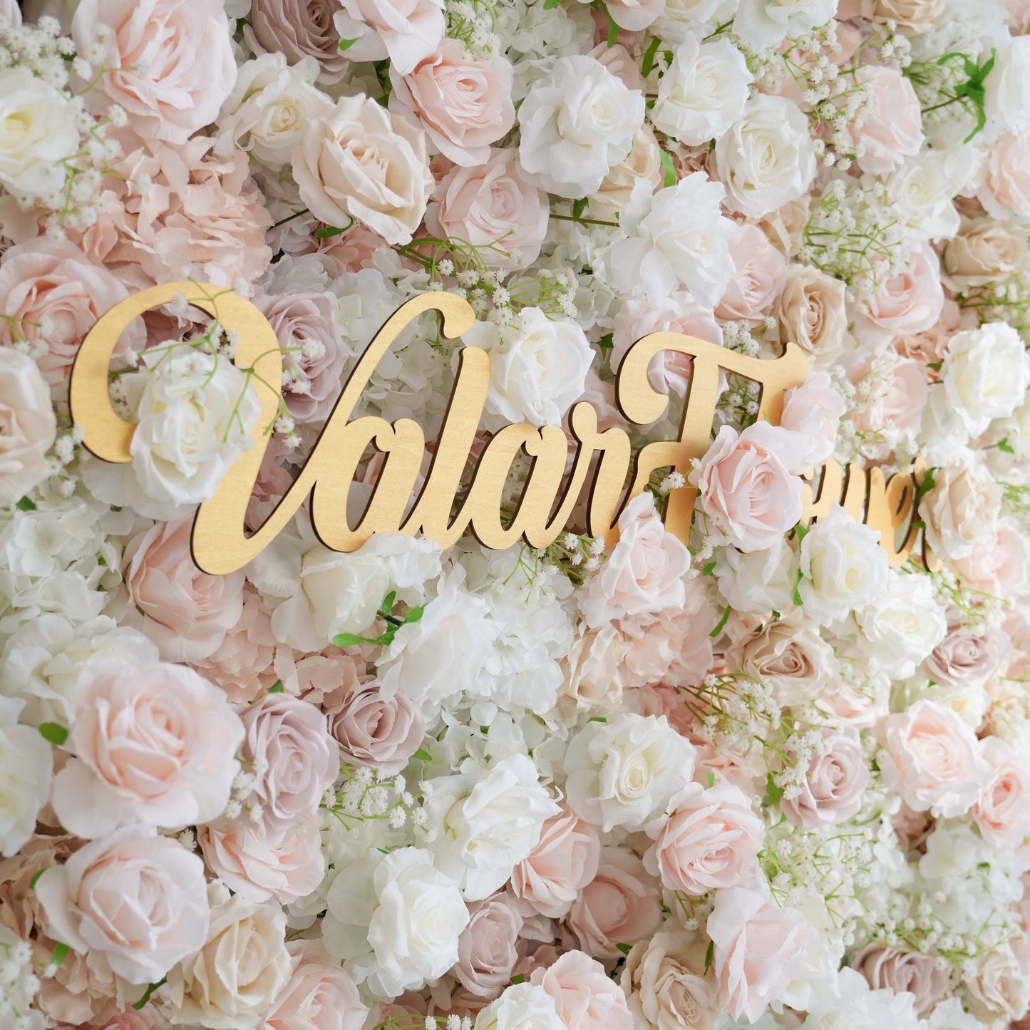 This floral backdrop is a dense arrangement of artificial flowers. It features roses in soft shades of pink, white, and blush, interspersed with delicate sprigs of baby's breath. The color palette is light and pastel - toned, creating a romantic and elegant style, perfect for wedding or event photo backdrops. The "ValarFlowers" sign adds a branded touch. 