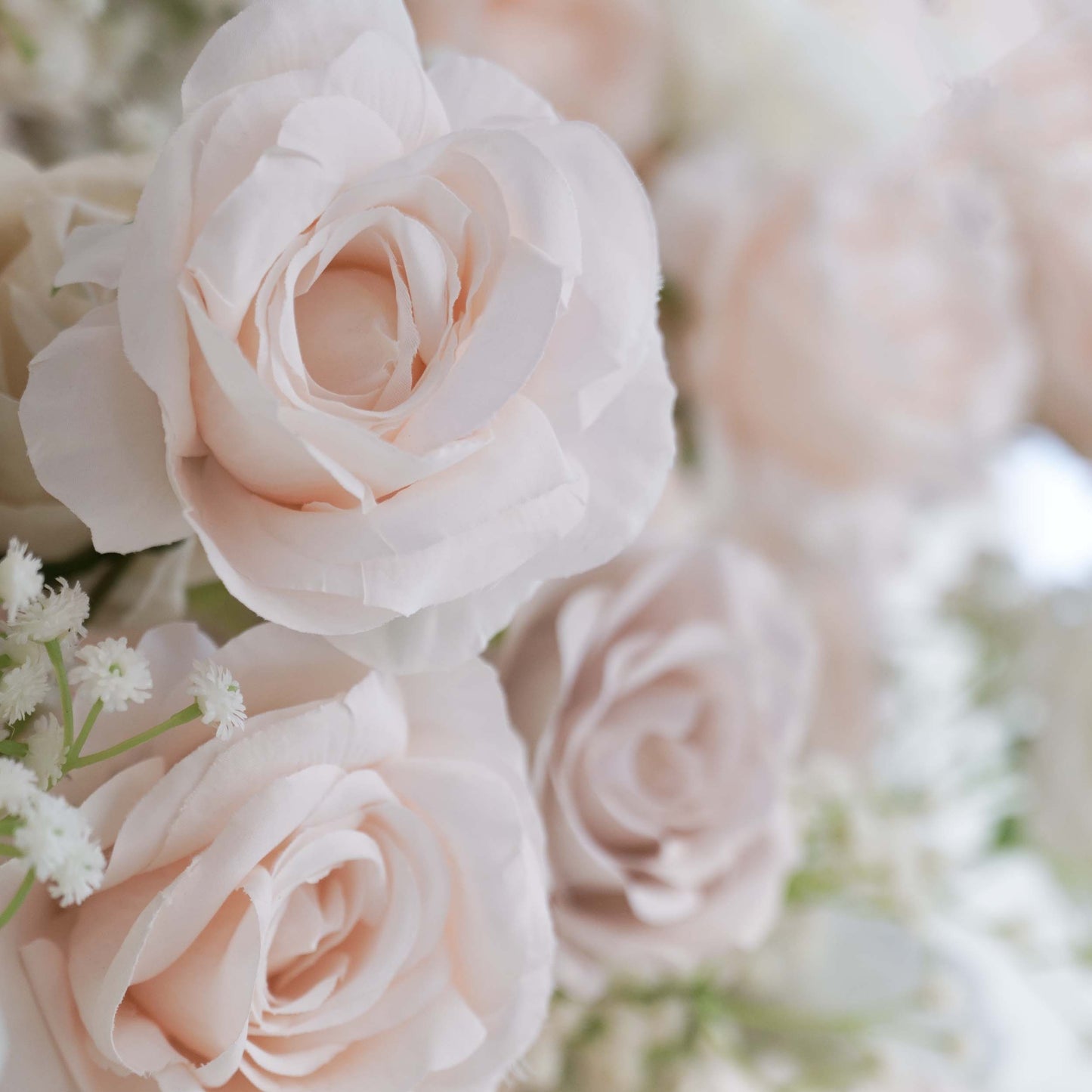 This close - up image highlights a section of a floral backdrop. The flowers predominantly include artificial roses in soft, pastel shades such as light pink and off - white. Delicate sprigs of baby's - breath - like greenery are interspersed among the roses. The overall color palette is gentle and soothing, creating a romantic and elegant style, perfect for wedding or event decorations. 